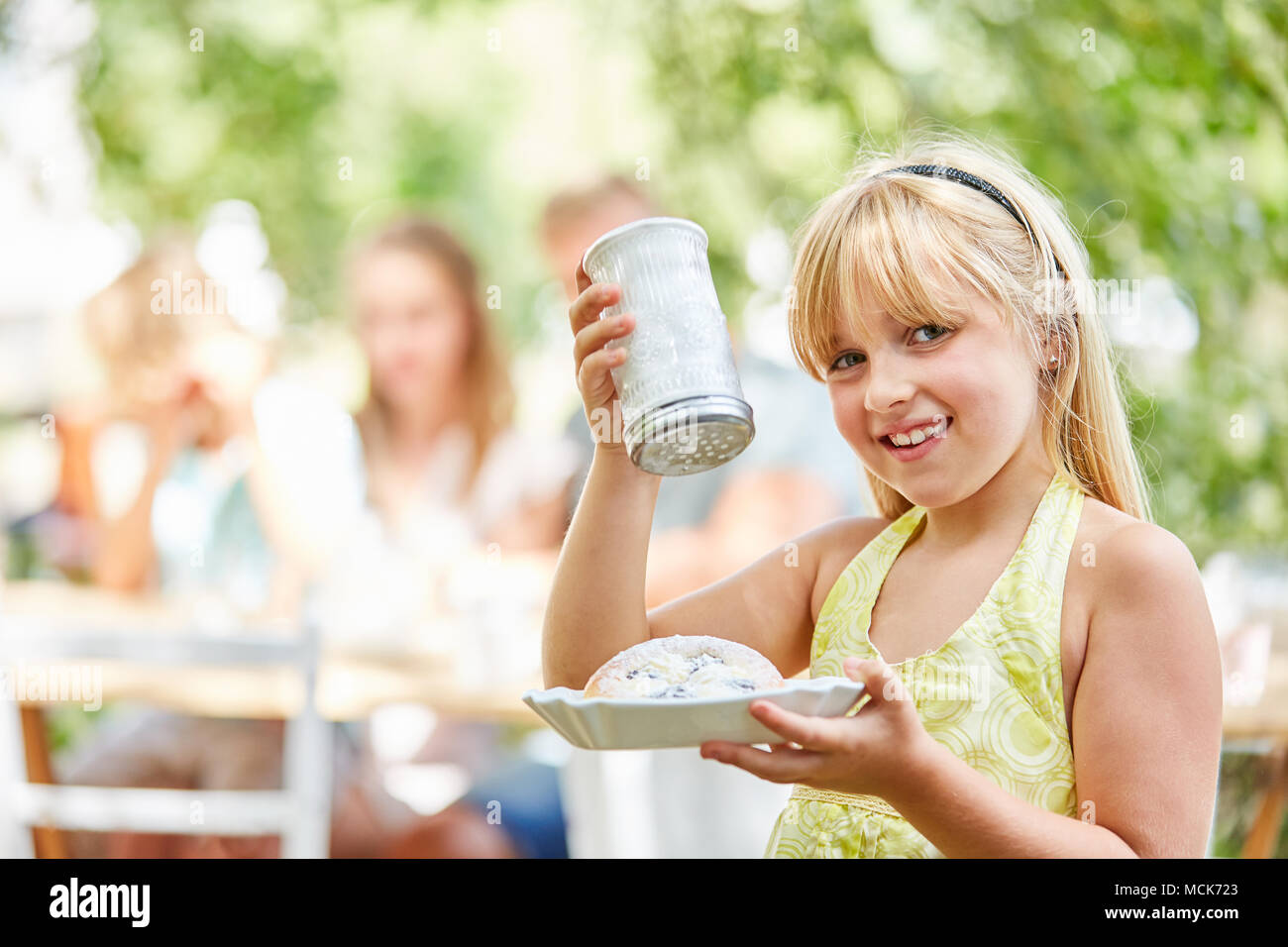 Blond girl with sugar shaker and cake in the garden in summer Stock Photo