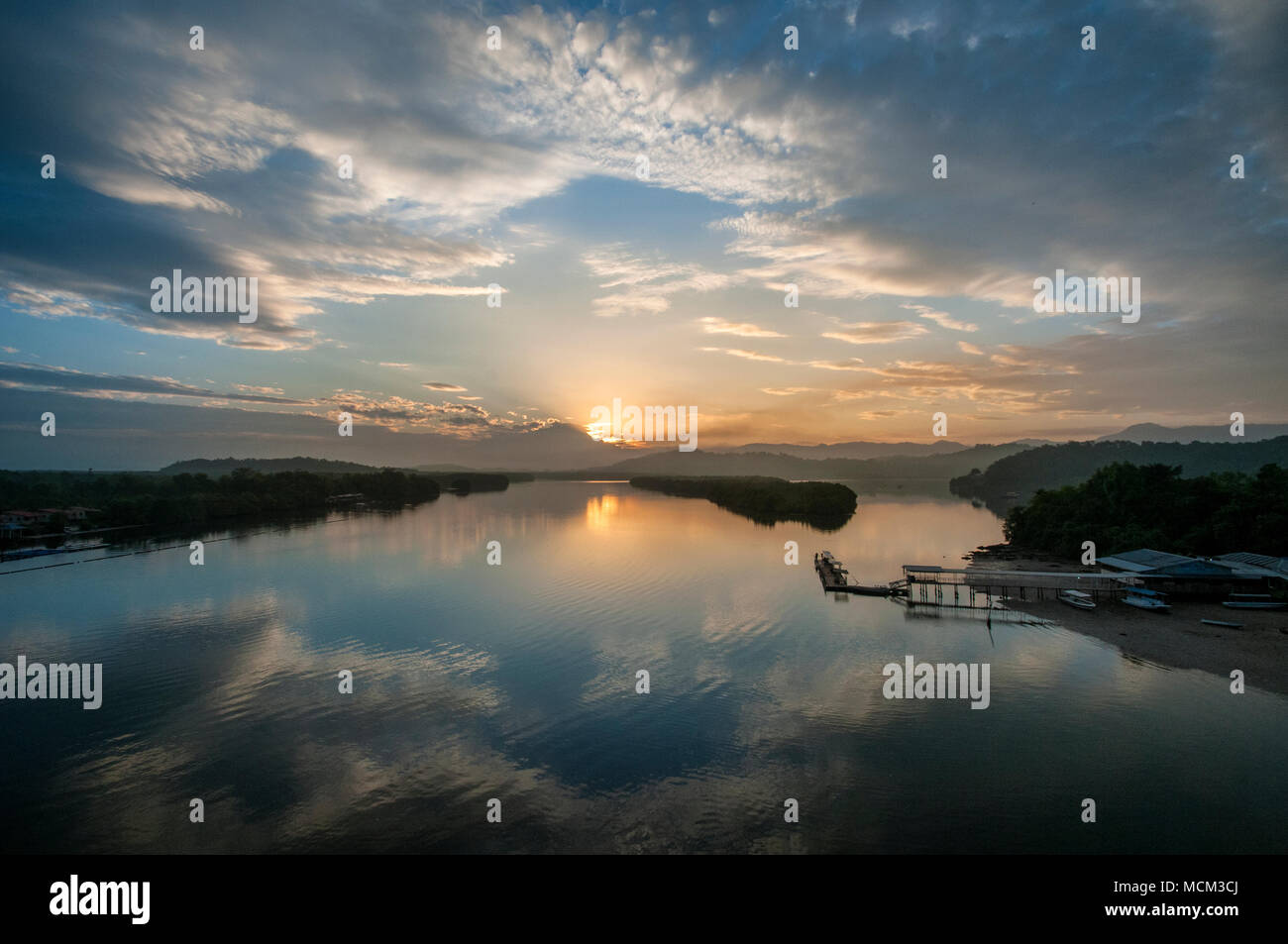 Beautiful and colorful sunrise shot from Mengkabong river with a boat passing under the bridge. Stock Photo