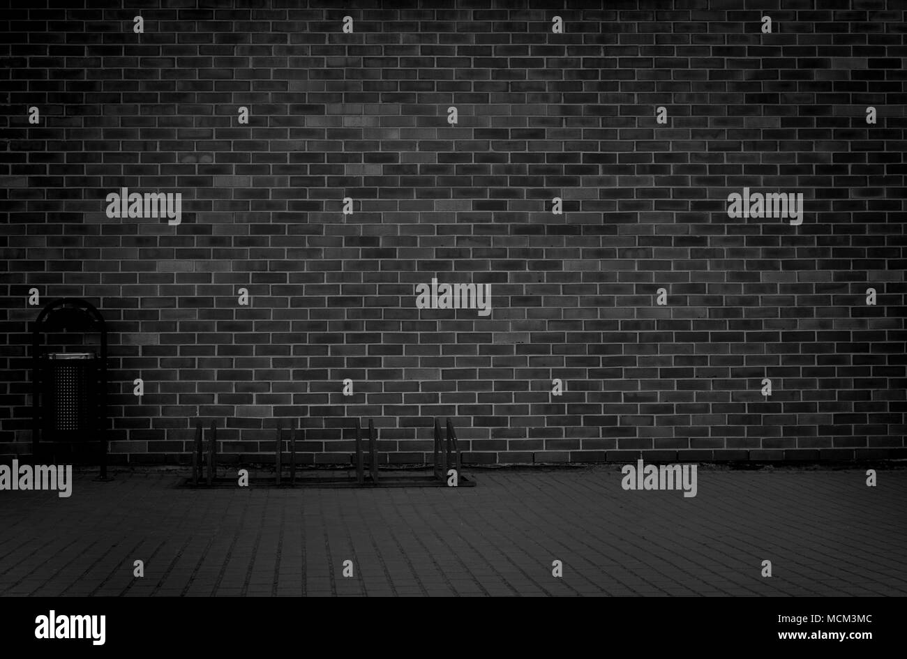 Brick grunge weathered black wall background with walkway and garbage can Stock Photo
