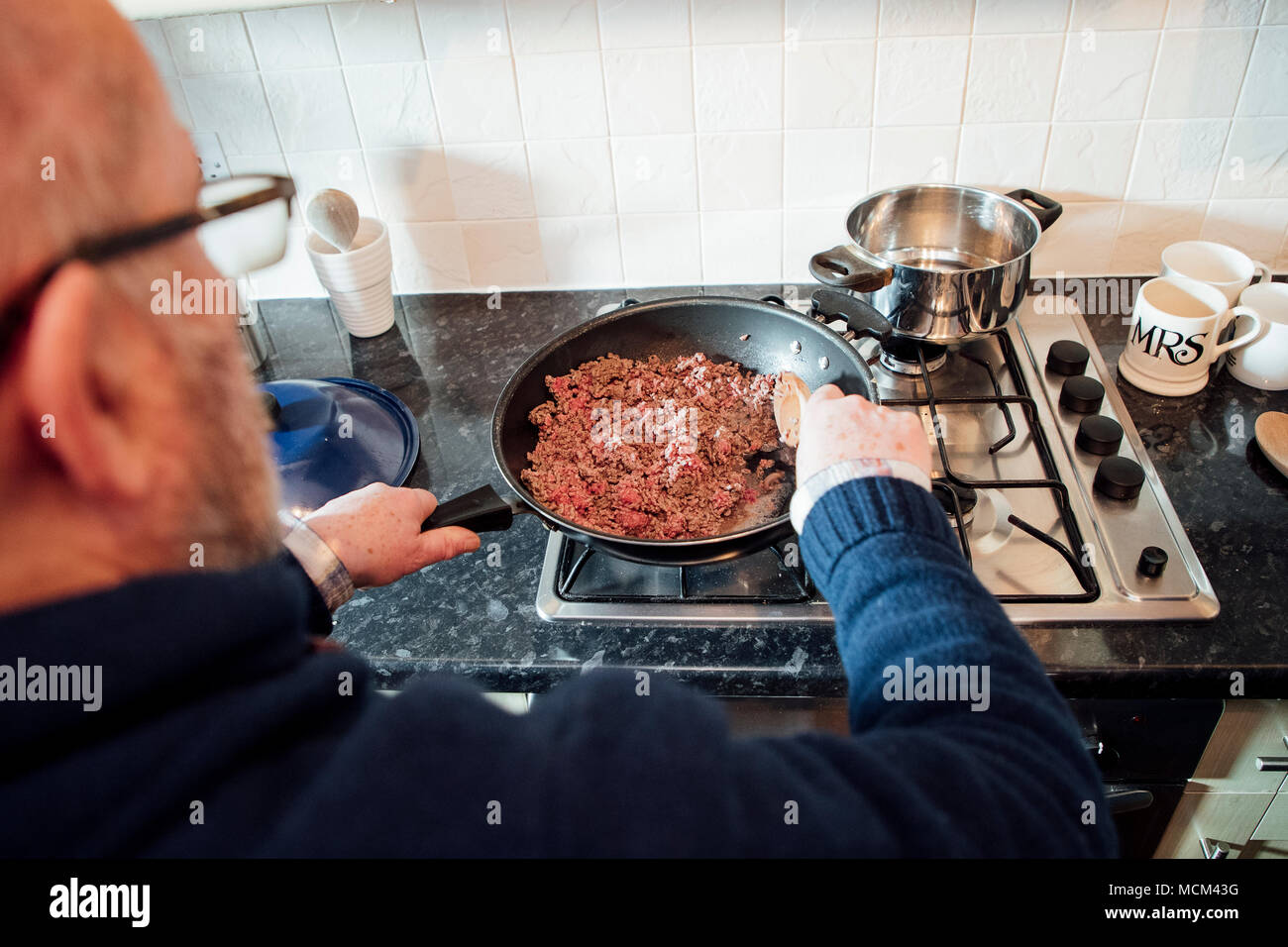 Over the shoulder shot of a mature man browning off mince to make a spagetti bolognese. Stock Photo