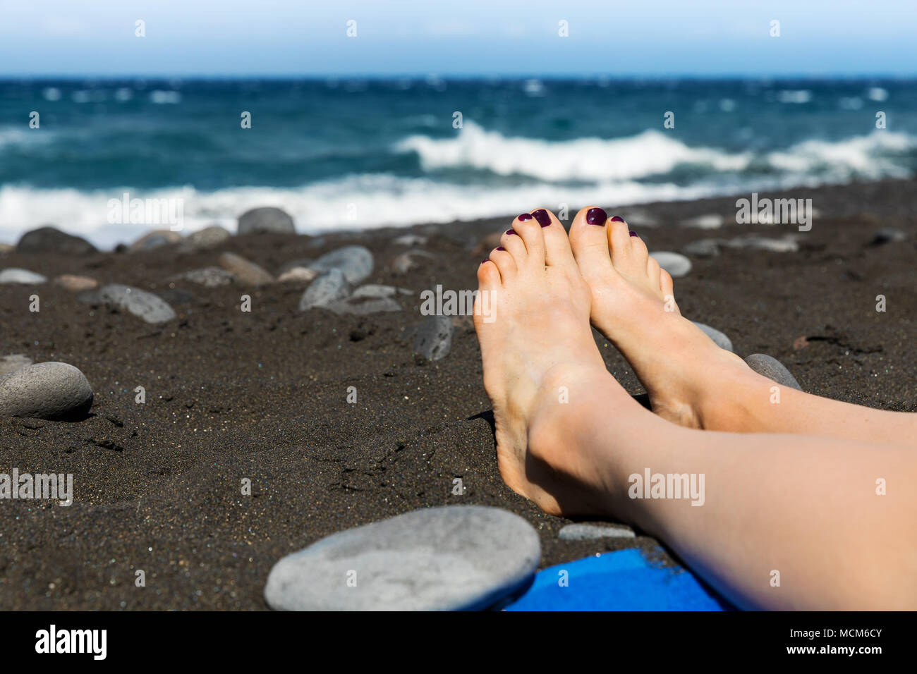 sunbathing - woman feet on black sand beach Stock Photo