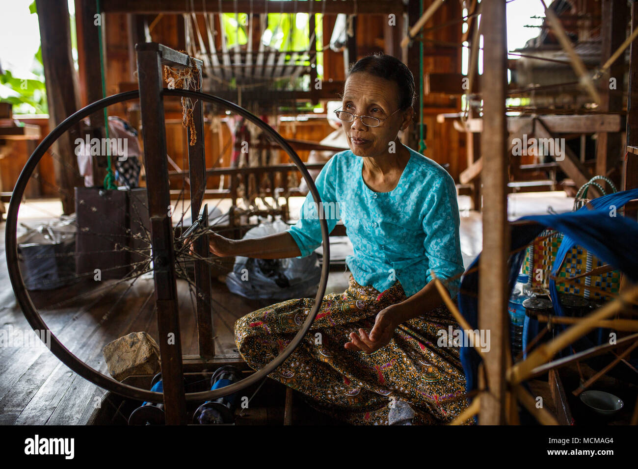 Senior woman weaving silk on spinning wheel inside house hires stock