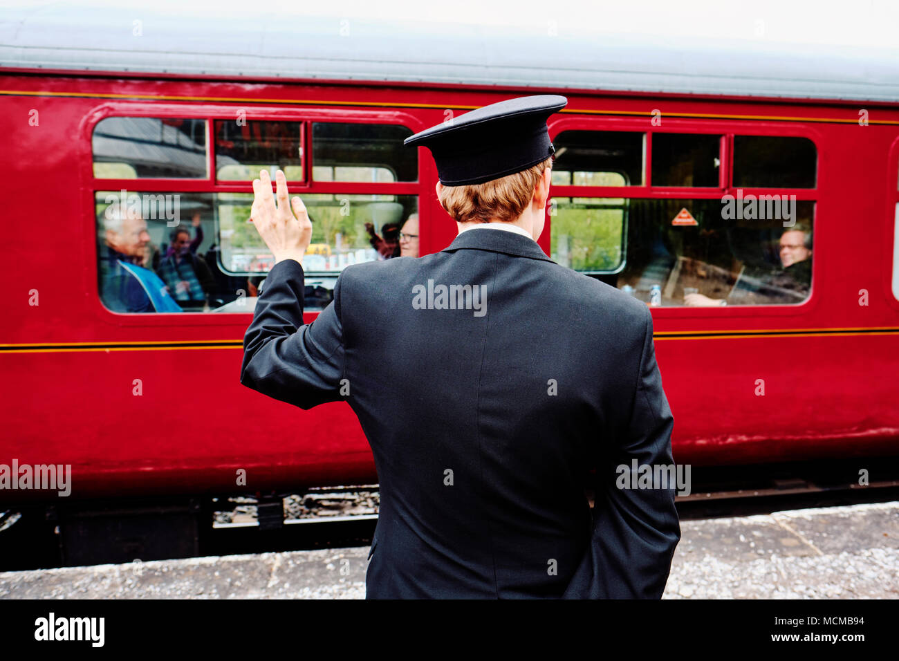 The station manager on a vintage steam railway line waves goodbye to passengers. Stock Photo