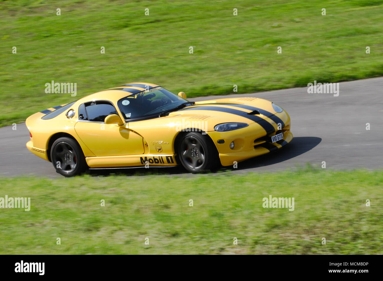 Yellow Dodge Viper American sports car with black racing stripes driving fast. Stock Photo