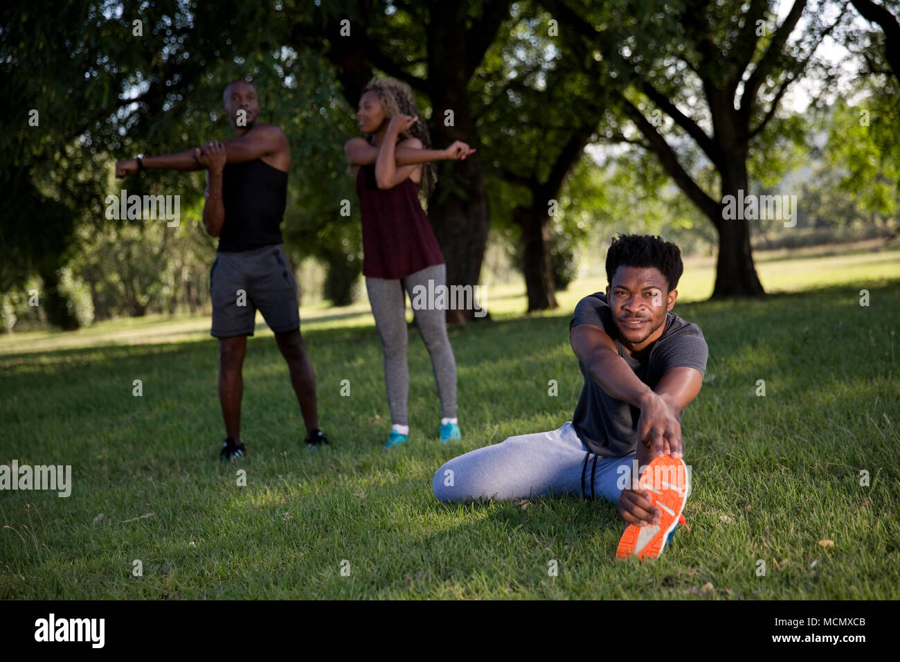 Two men and woman stretching in a park Stock Photo