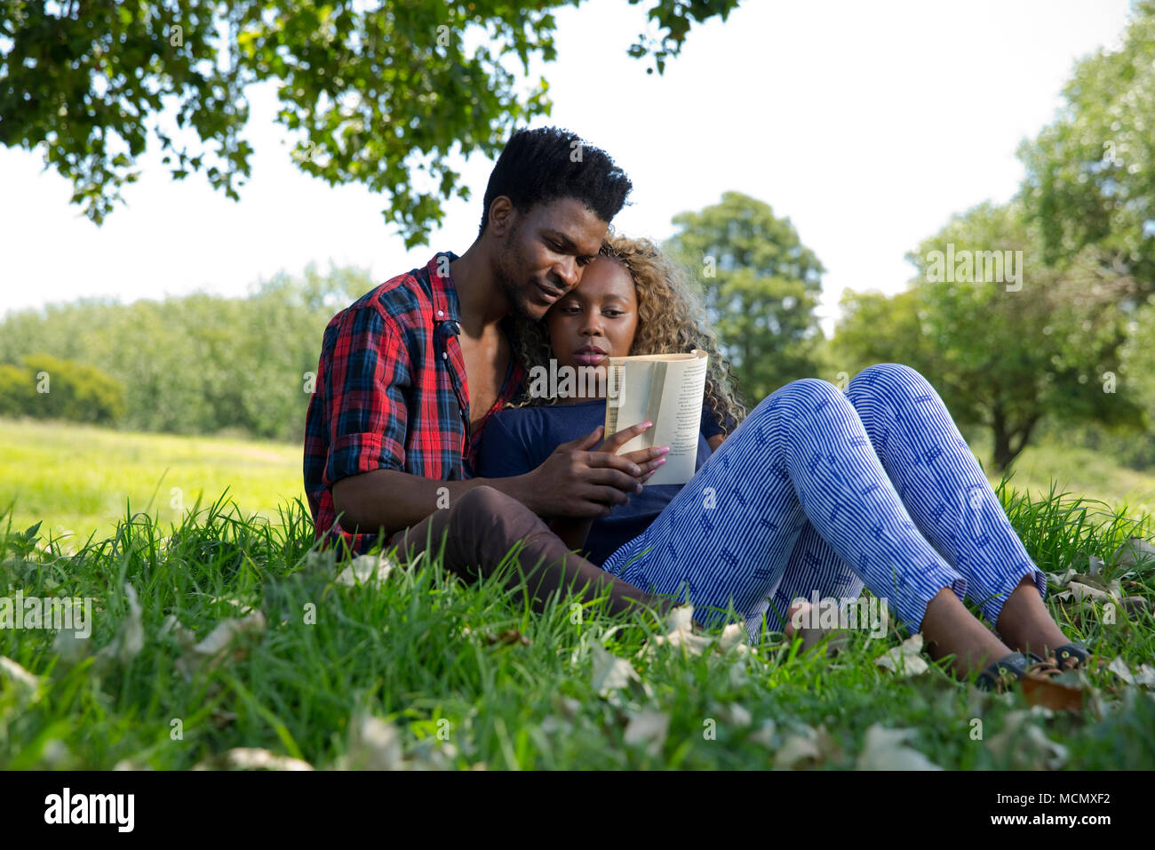 Couple cuddling and reading a book in a park Stock Photo