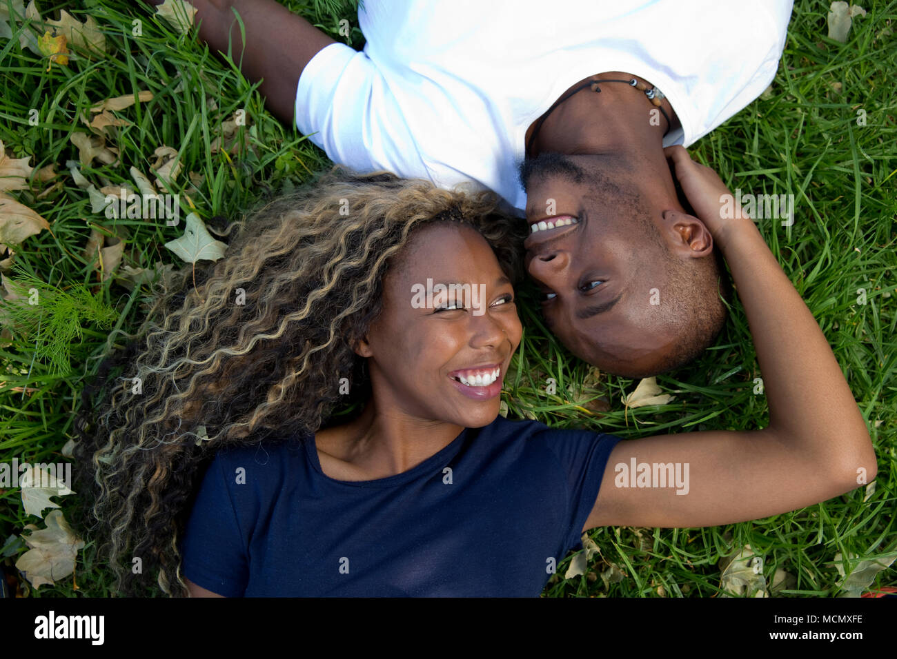 Couple lying on the grass looking into each other's eyes Stock Photo