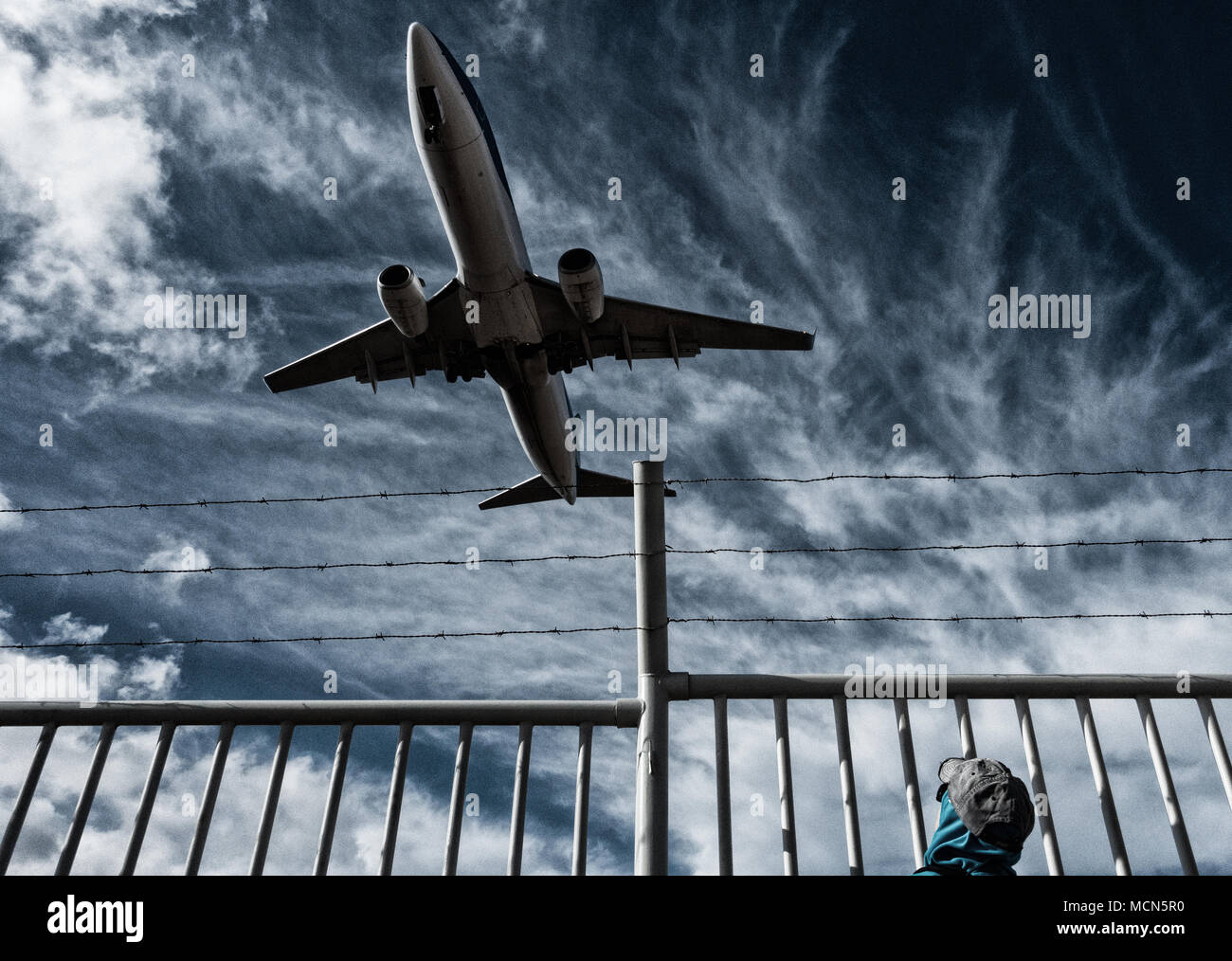 Woman watching aircraft/airplane from behind barbed wire perimeter, border fence. Concept image: Russia Ukraine conflict, no fly zone, refugee crisis. Stock Photo