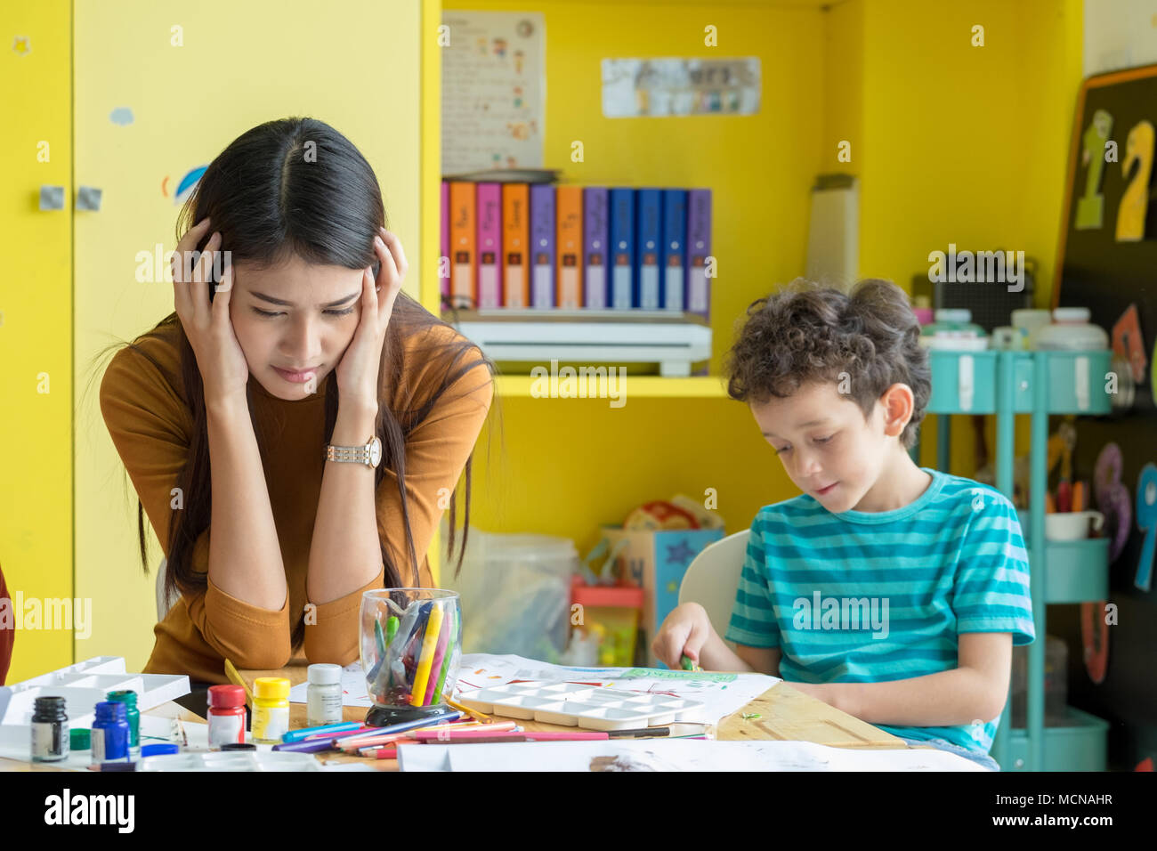 Asian woman teacher get headache with naughty boy kids in classroom at kindergarten pre school. Uncontrolled behaviour Stock Photo