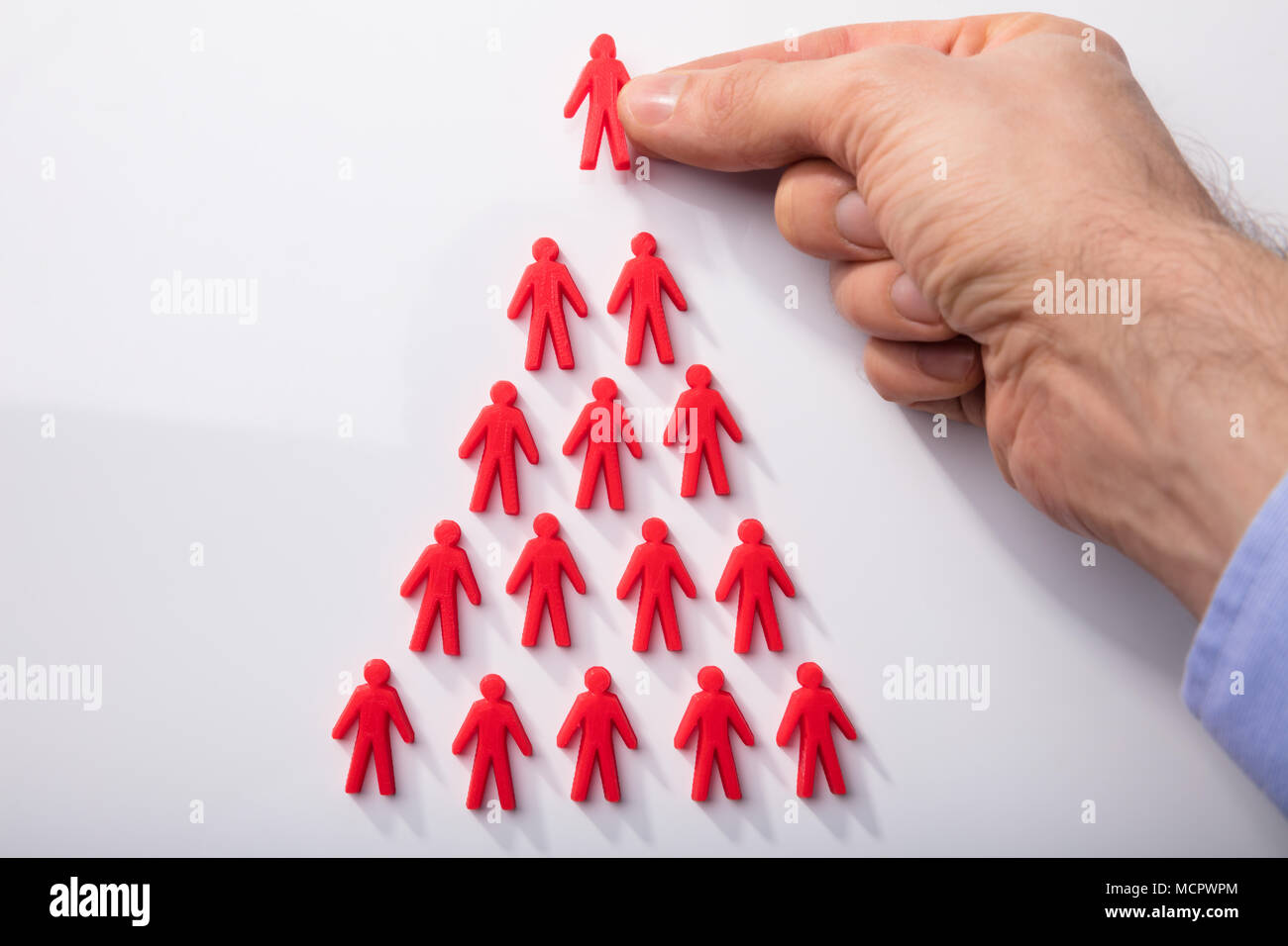 Close-up Of A Person's Hand Arranging Red Human Figures In Triangular Shape On White Background Stock Photo