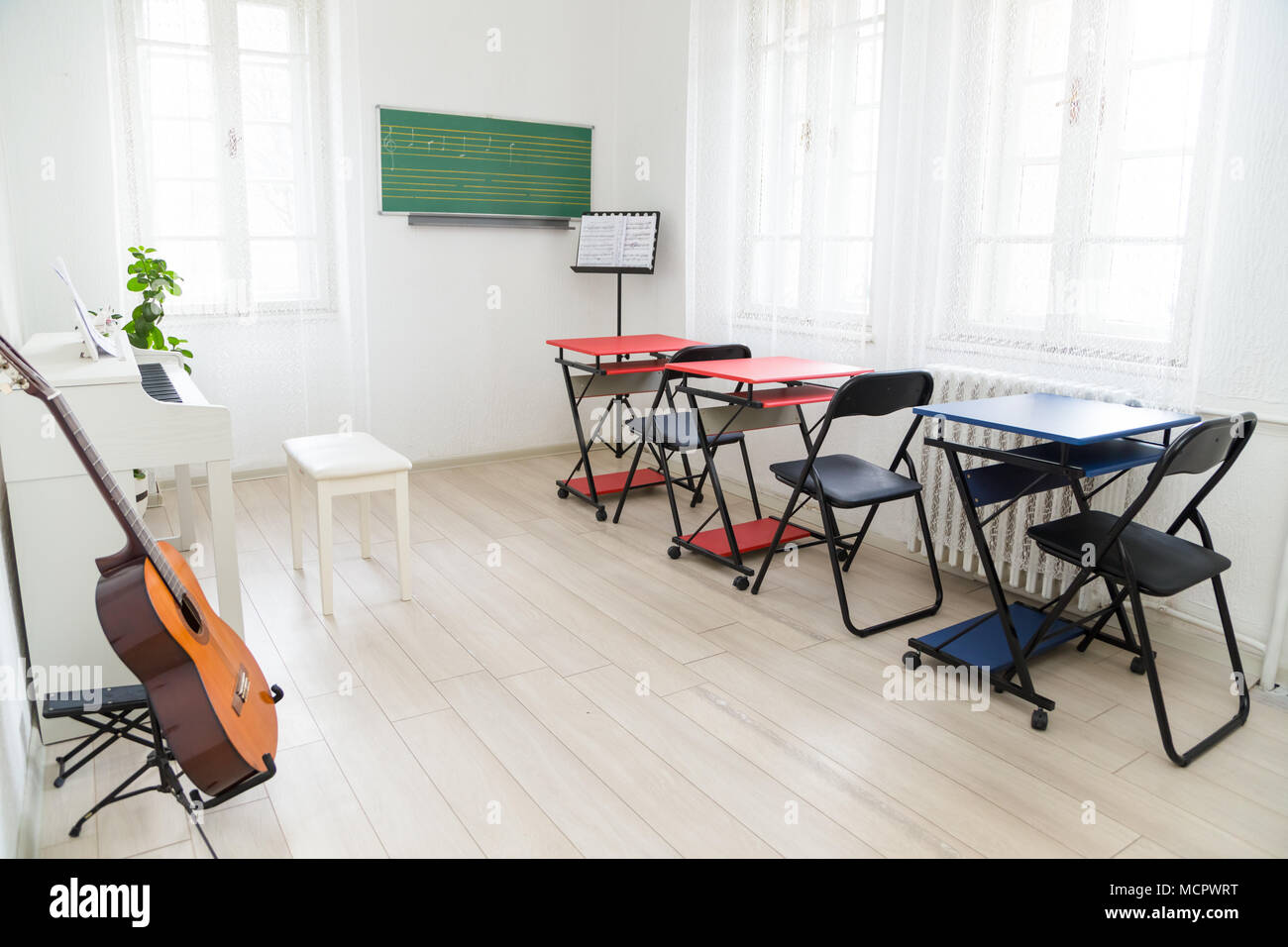 Modern daylight classroom for teaching music. Guitar, white piano and greenboard in modern music classroom Stock Photo
