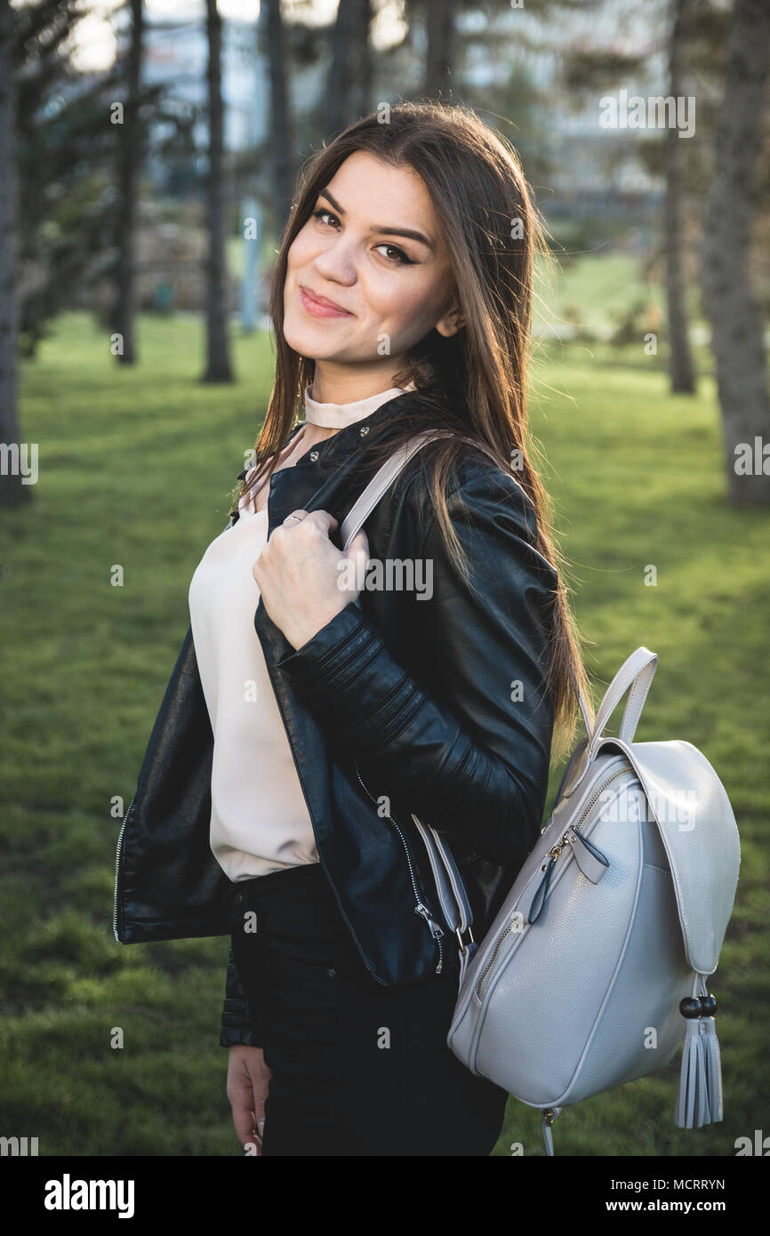 A portrait of a girl in the park holding a small leather backpack on the shoulder Stock Photo