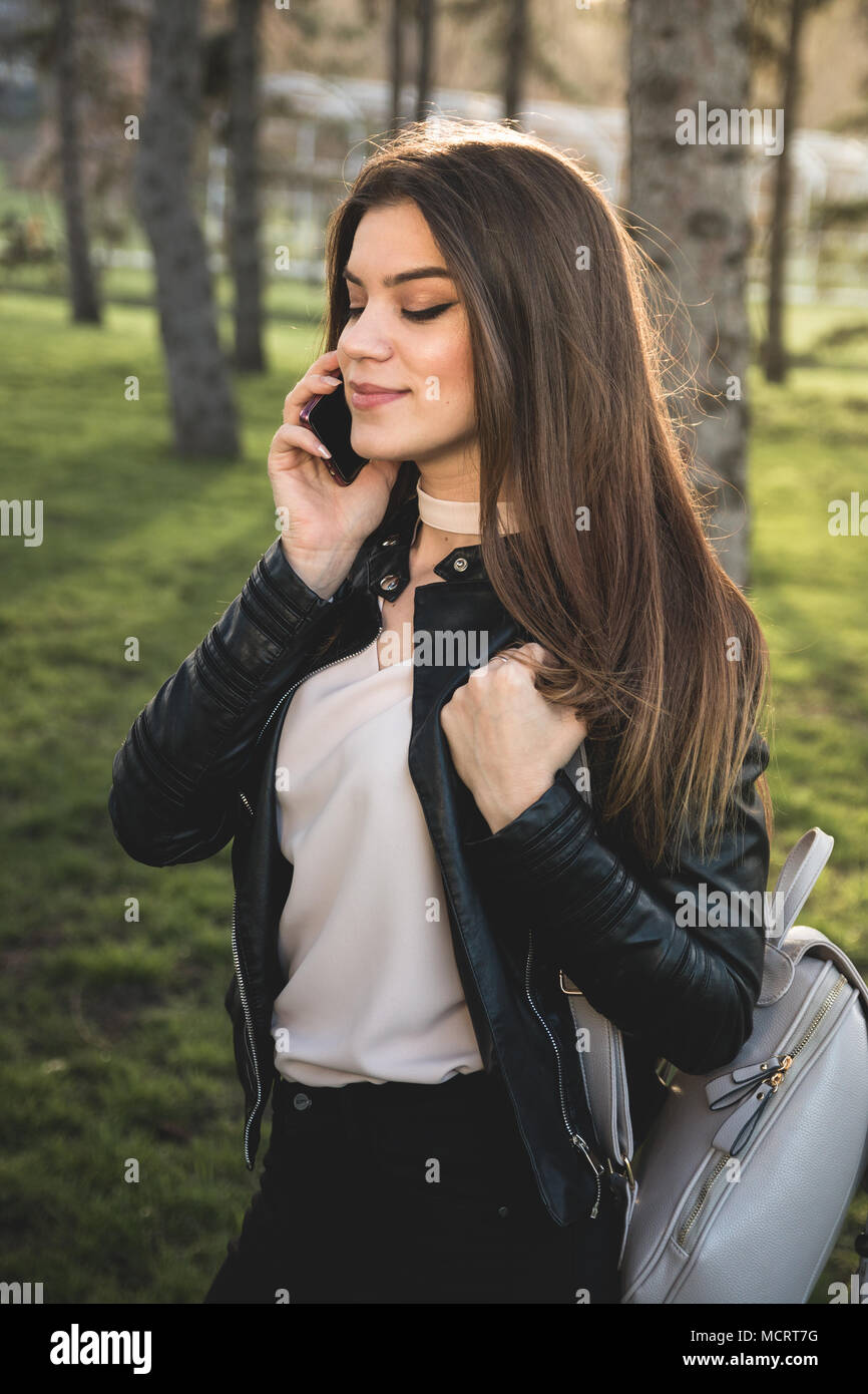 Girl speaking on the phone and bag on shoulder in the park at sunset, make up on Stock Photo