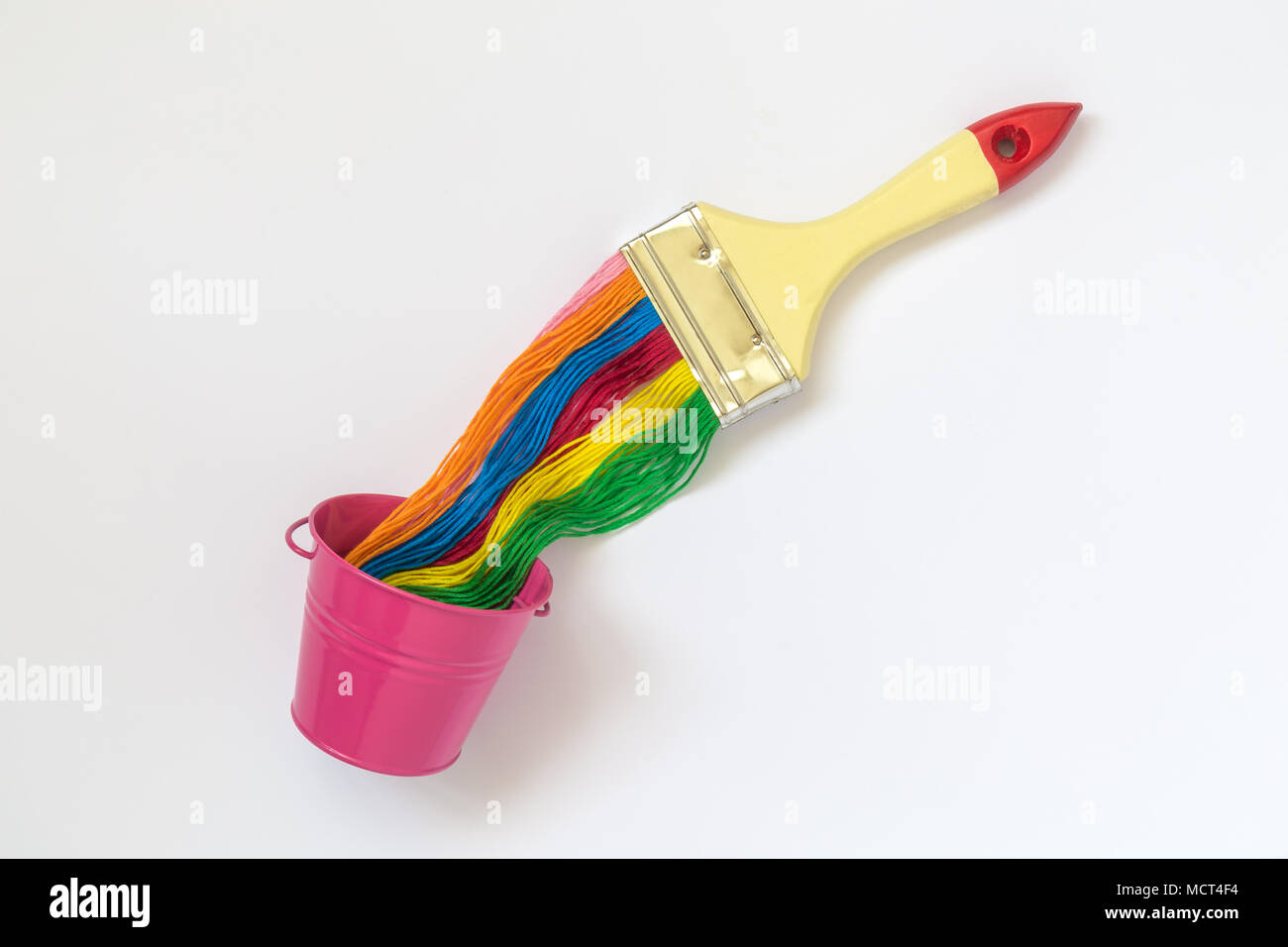 Paint brush with colorful strings and small pink bucket on white