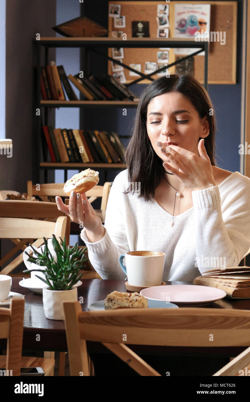 Girl in a cafe holding a doughnut and licking her fingers Stock Photo