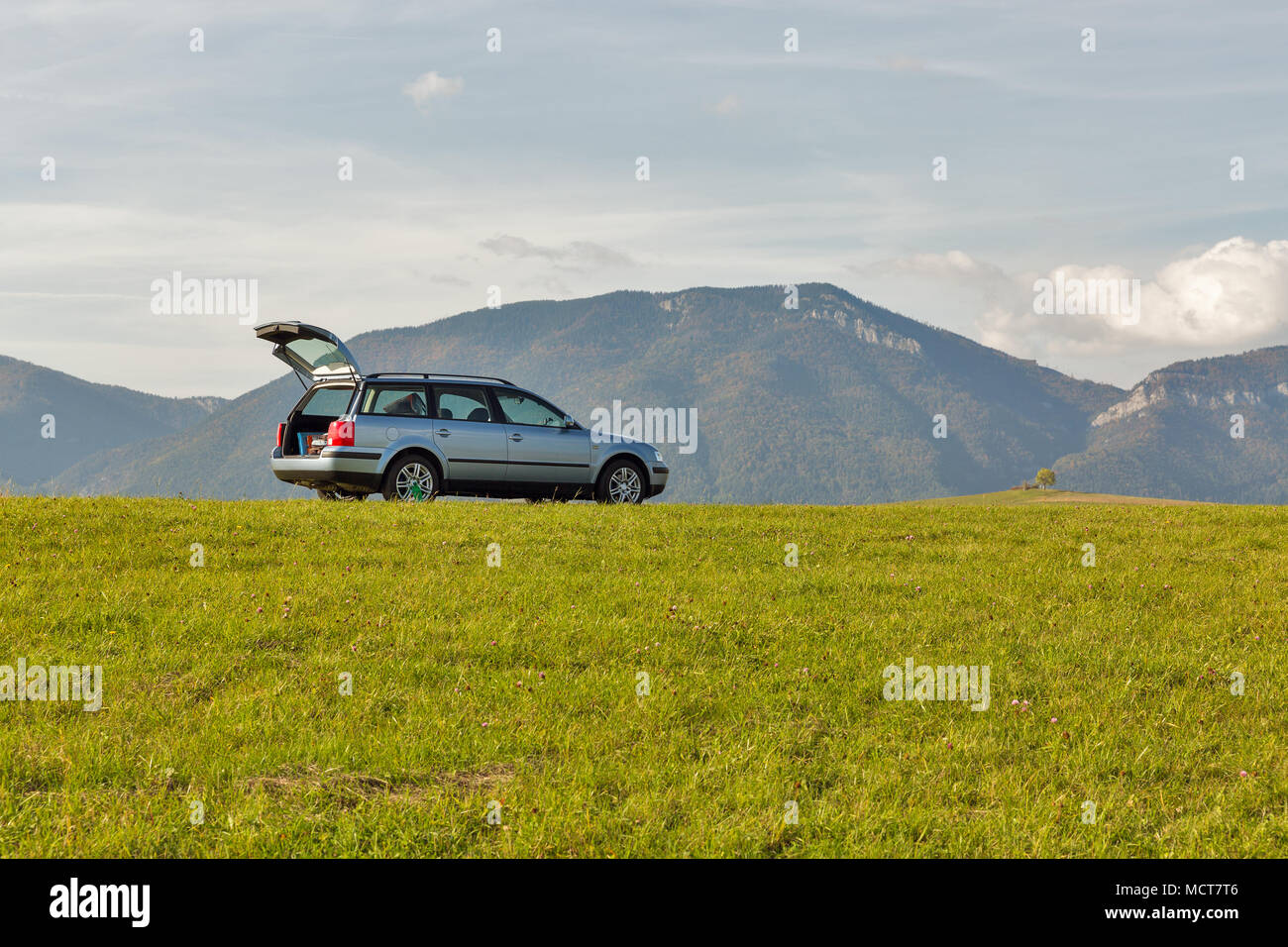 hatchback car with open trunk on the top of the summer hill. blue sky