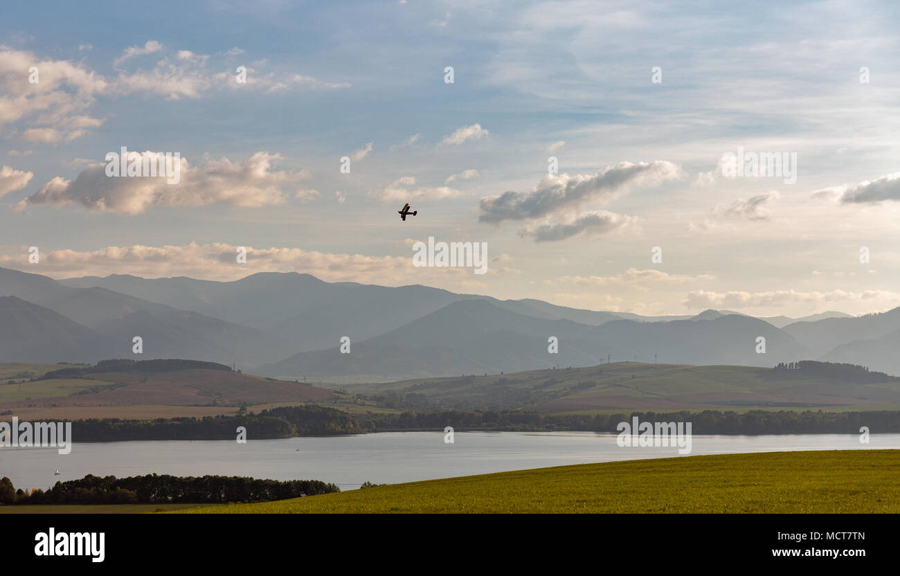 Small retro biplane fly over summer hills landscape and Liptovska Mara lake close to Liptovsky Trnovec village in Slovakia. Stock Photo