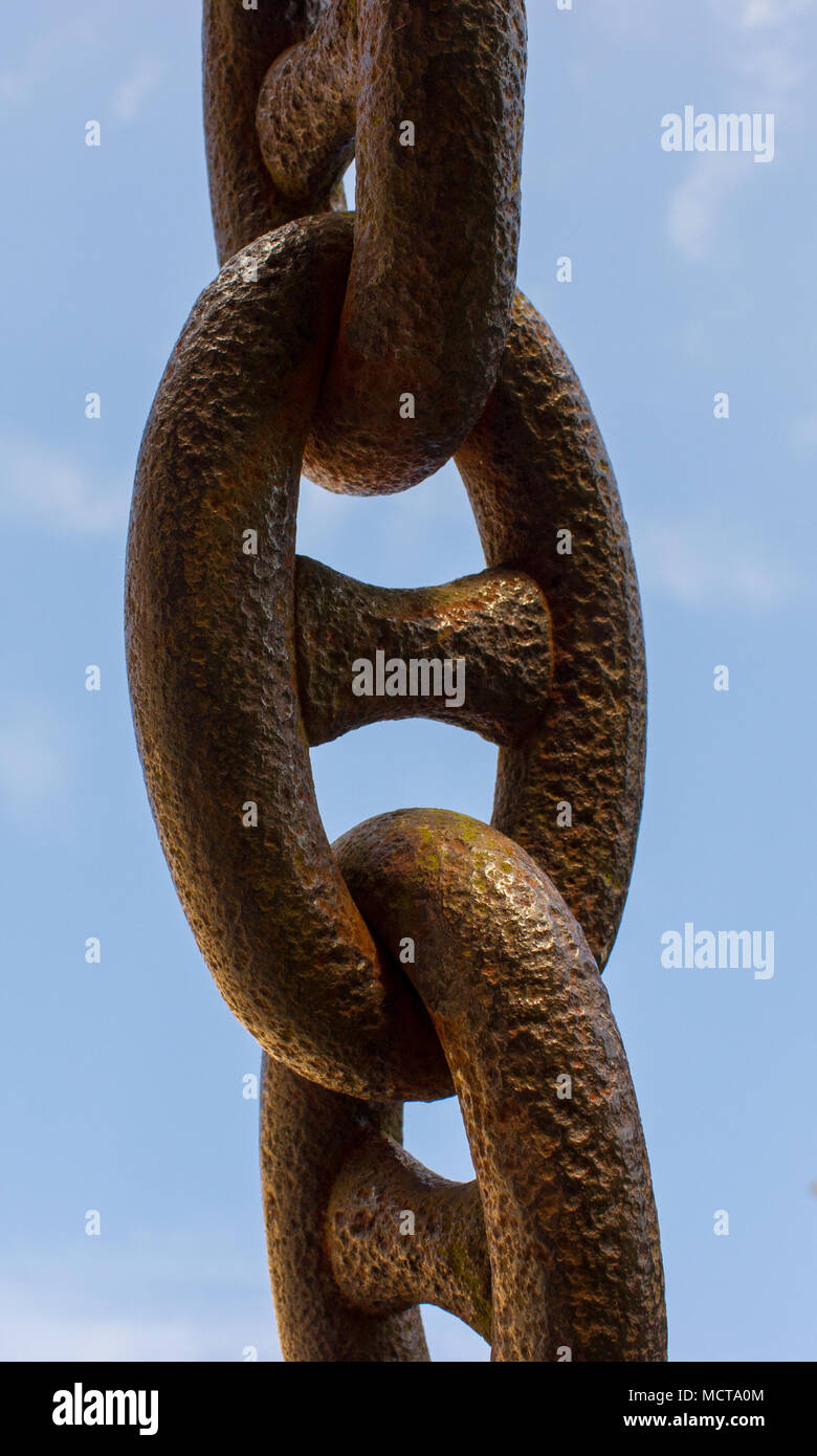 An old rusty chain on a blue background. In the background is blue sky with white clouds. Stock Photo