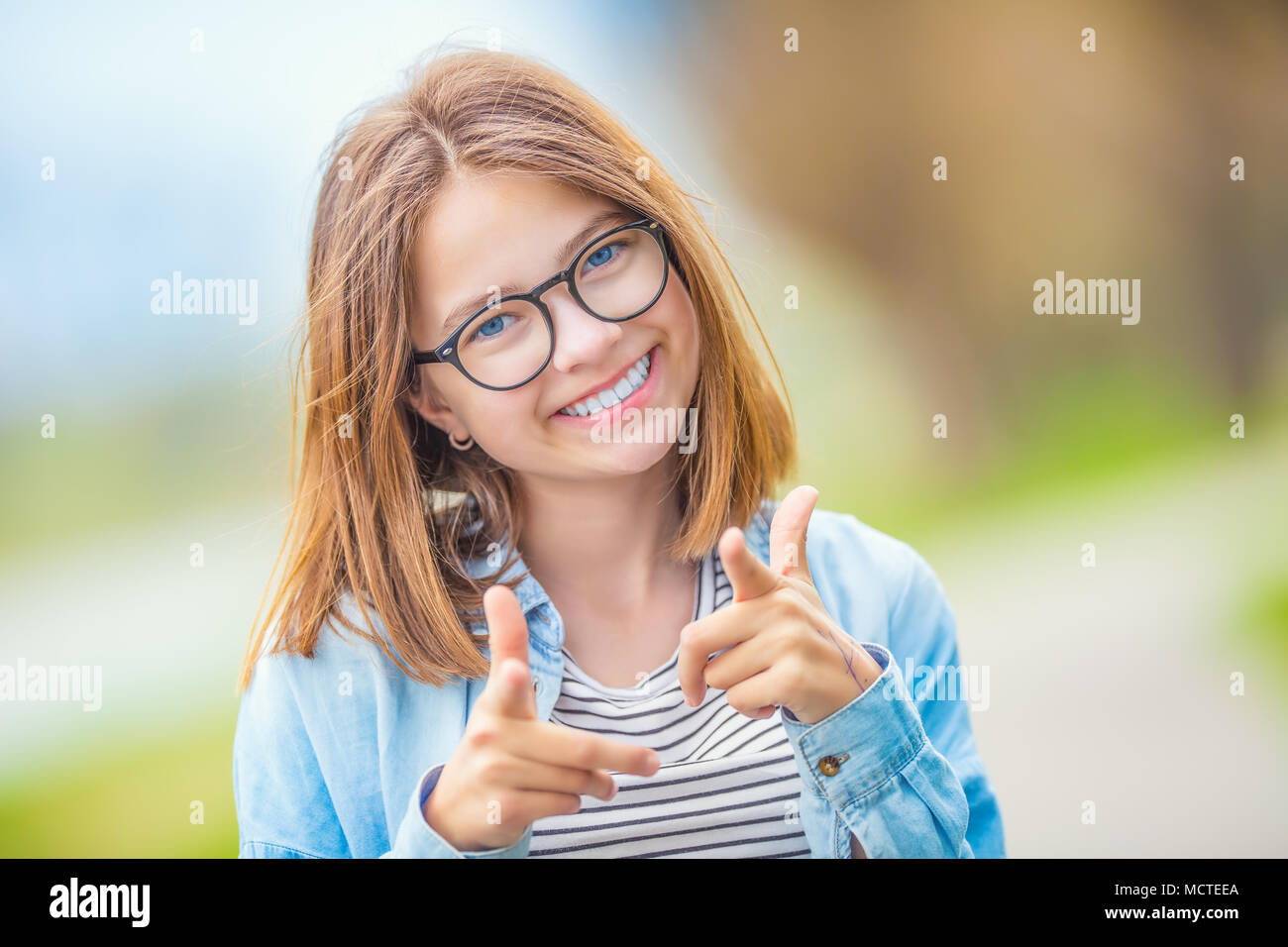 Portrait of happy smilling teenage young girl with glasses and beautiful smile showing with enthusiasm to you. Stock Photo