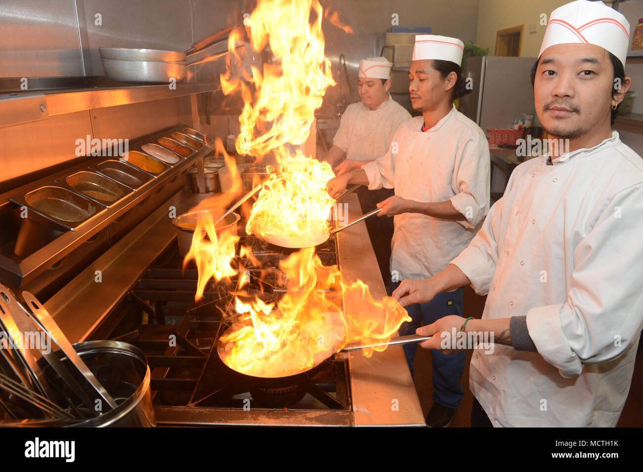 Three chefs cooking on a cooker in a restaurant making flames while they are cooking Stock Photo