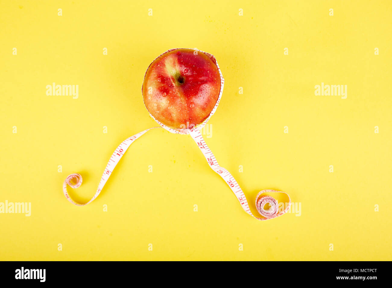 Measuring tape wrapped around a red apple as a symbol of diet on yellow paper background. Weight loss concept. Diet. Dieting concept. Vegan. Clear foo Stock Photo