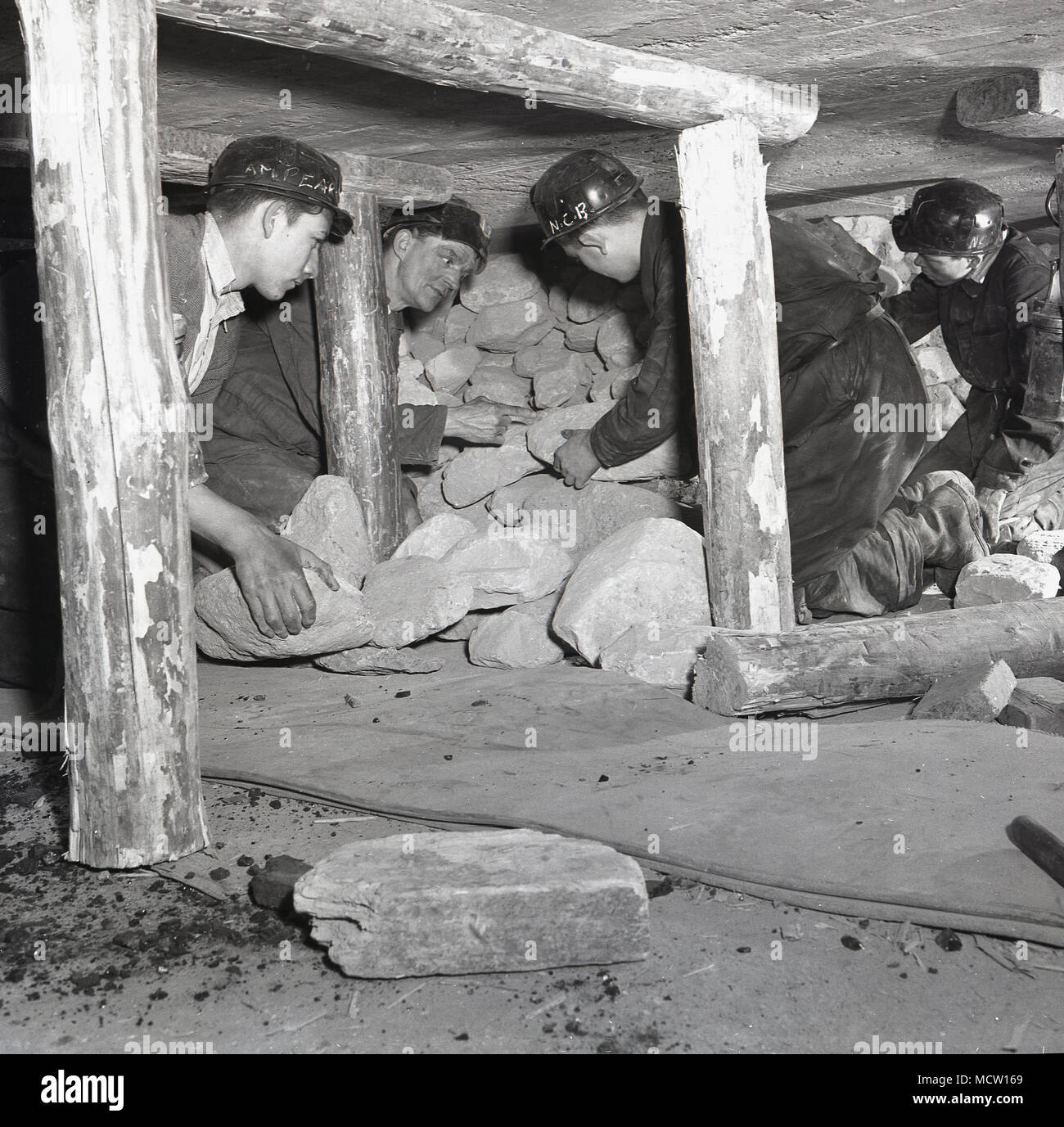 1950s, historical, Mining student being shown how to remove rocks safely in a confined underground coalmine, with its roof supported by timber beams on wooden props.  England, UK. in post-war Britain, mining was still an important industry with over 500 pits in existence and the government of the day actively encouraged young people to gain mining knowledge and skills and to enter the industry. Stock Photo