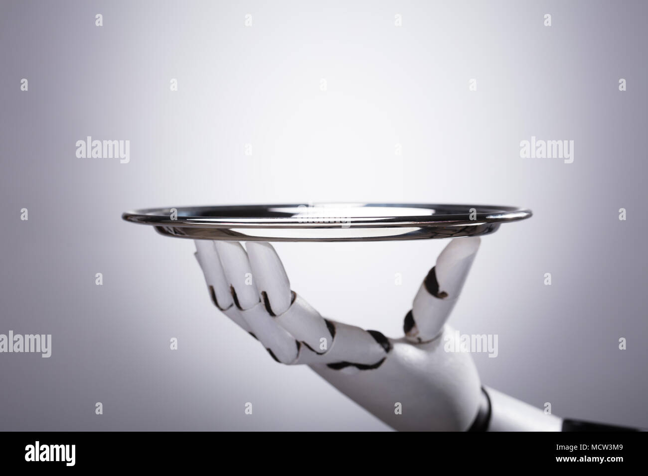 Robot Hand Holding Empty Plate Against Grey Background Stock Photo
