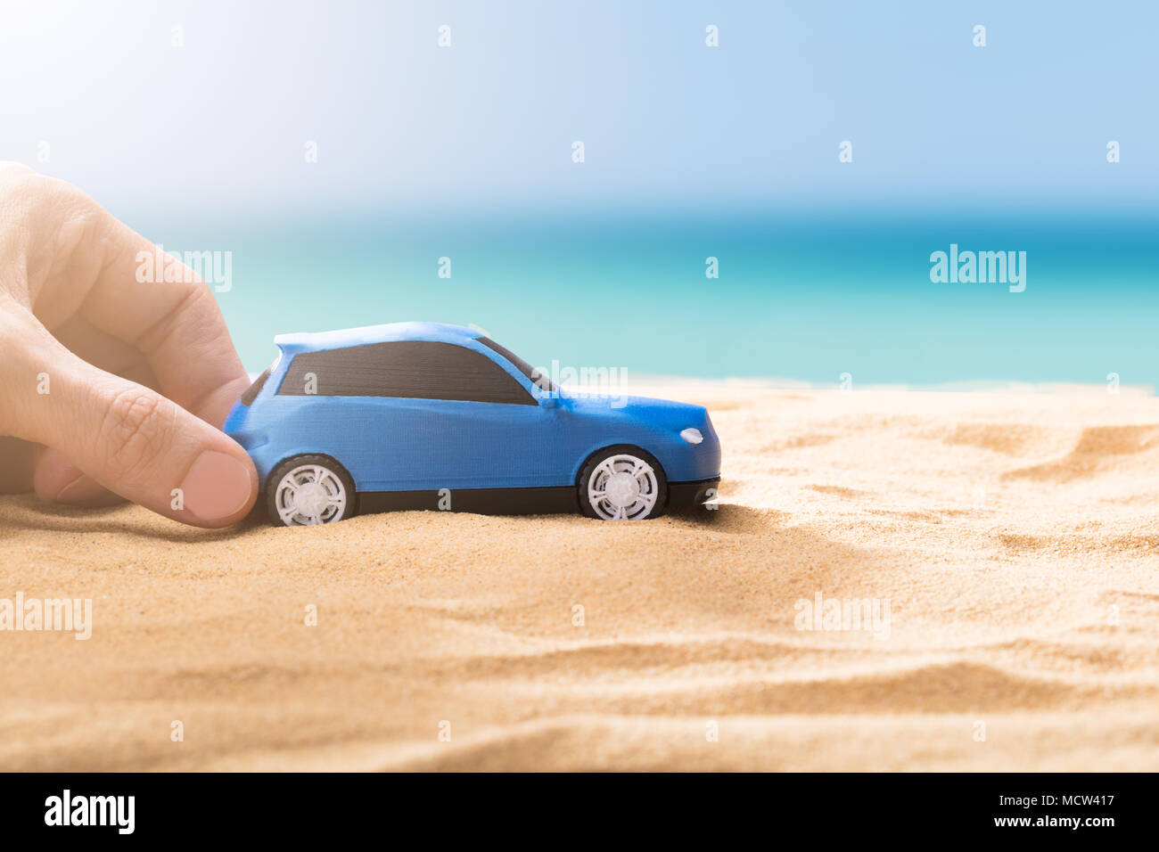 Human Hand Holding Small Blue Car On Sandy Beach Stock Photo