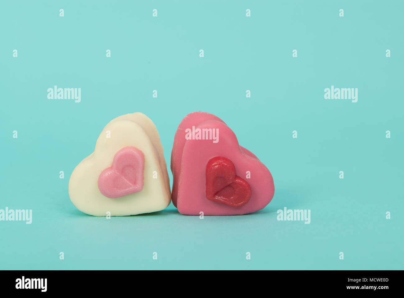 Two heart sheaped pink petit four candy's on a turquoise background Stock Photo