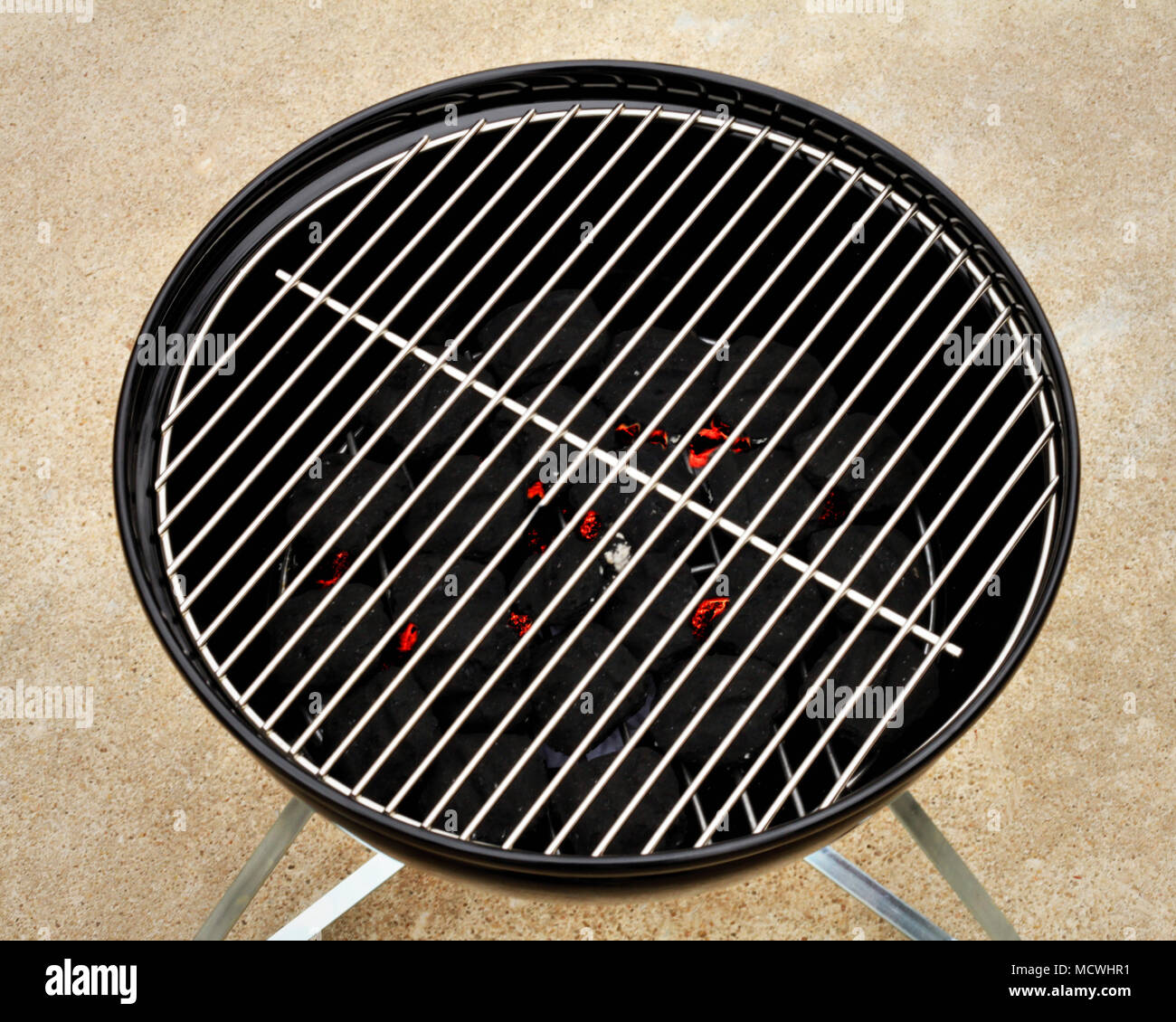 Embers begin to glow under the grate of a small barbecue grill. Stock Photo