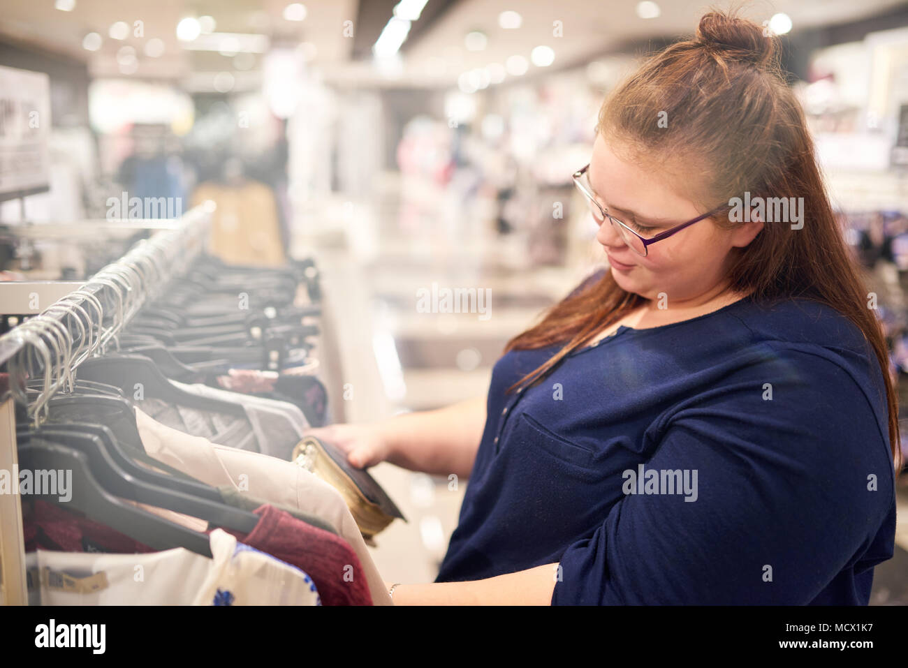 Bigger white girl busy looking for the perfect outfit while shopping in a mall by herself for a formal work function she has to attend in formal attire. Stock Photo
