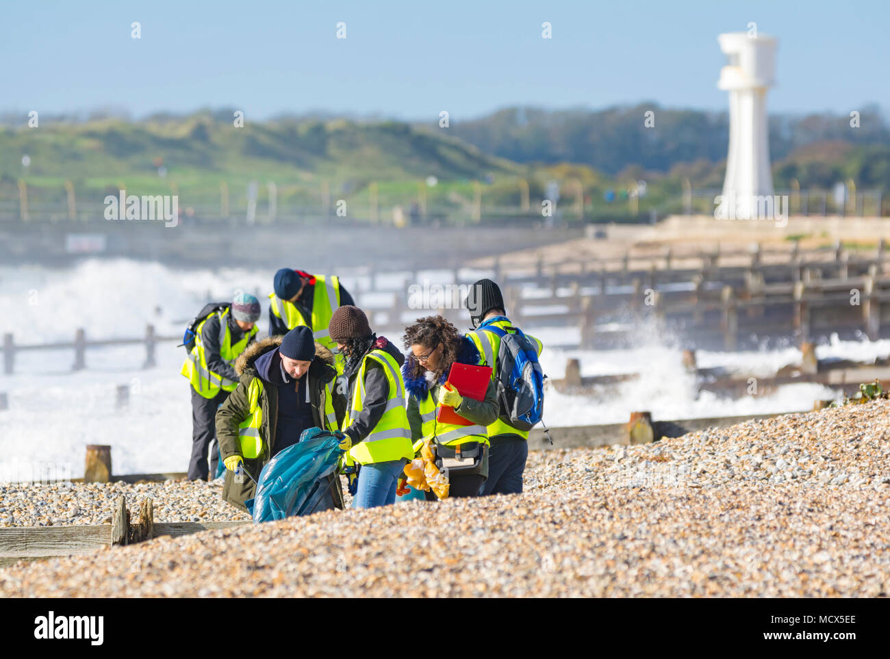 Group of people on a beach picking up litter. People removing rubbish from a beach in the UK. Stock Photo