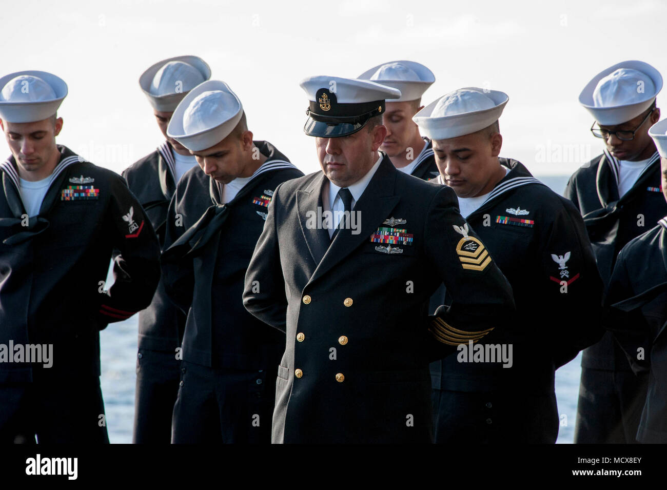 180304-N-HT134-022 PACIFIC OCEAN (March 4, 2018) Sailors aboard the amphibious assault ship USS America (LHA 6) bow their heads for the chaplain’s benediction during a burial-at-sea ceremony on the ship’s starboard elevator. America is underway off the coast of southern California preparing for an ammunitions offload prior to entering a planned maintenance availability period. (U.S. Navy photo by Mass Communication Specialist Seaman Daniel Pastor/Released) Stock Photo