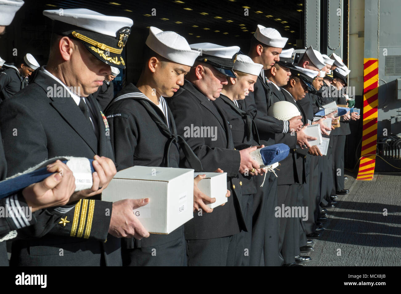 180304-N-ZS023-009  PACIFIC OCEAN (March 4, 2018) Sailors assigned to the amphibious assault ship USS America (LHA 6) bow their heads for the chaplain’s benediction during a burial-at-sea ceremony on the ship’s starboard elevator. America is underway off the coast of southern California preparing for an ammunitions offload prior to entering a planned maintenance availability period. (U.S. Navy photo by Mass Communication Specialist 3rd Class Vance Hand/Released) Stock Photo