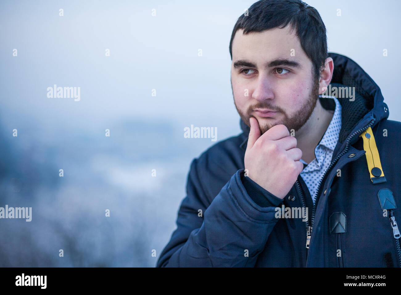 Portrait of a young thoughtful pensive man keeping hand on chin Stock Photo