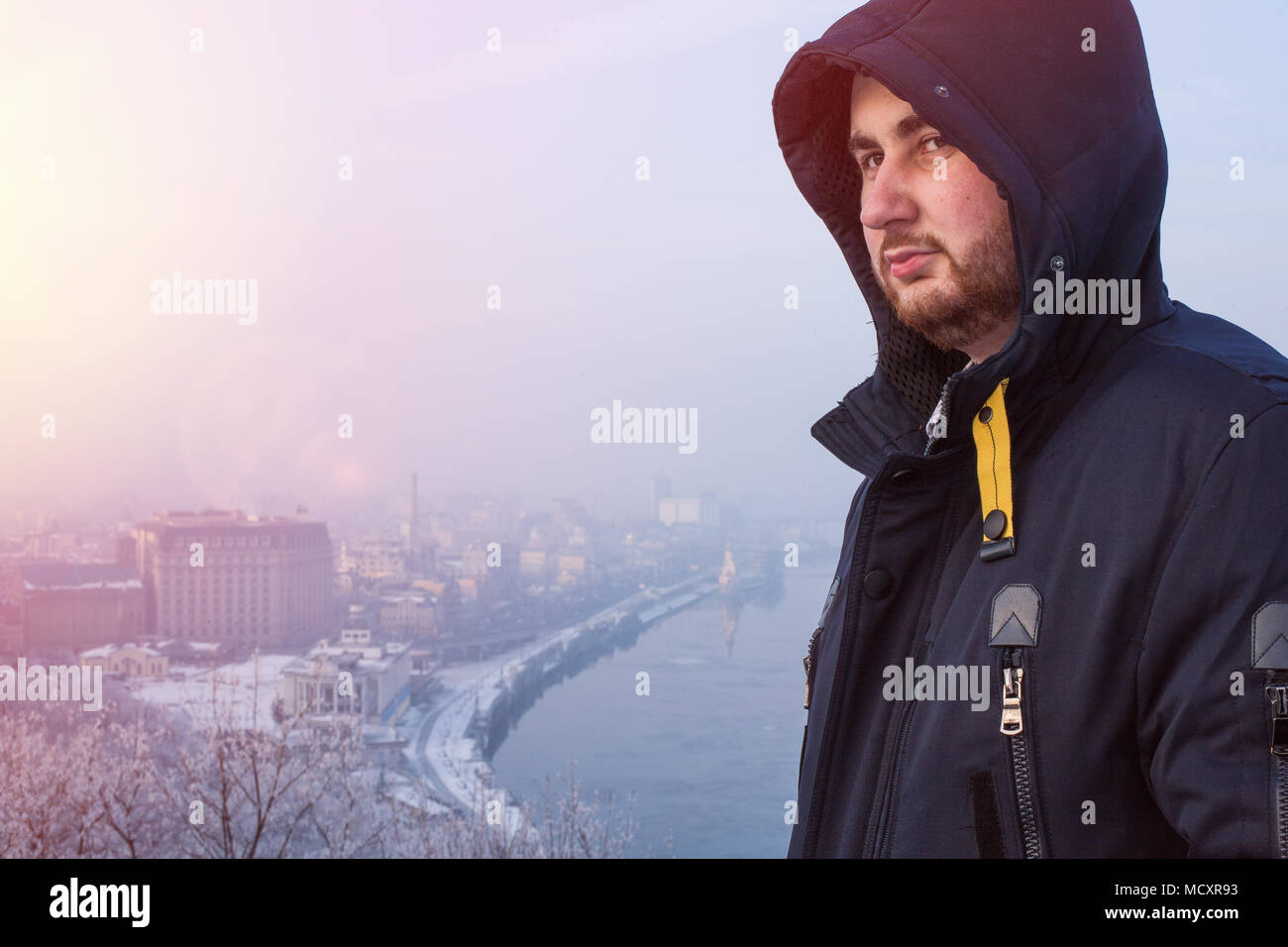 Portrait of a serious bearded man in hood against winter cityscape at sunset Stock Photo