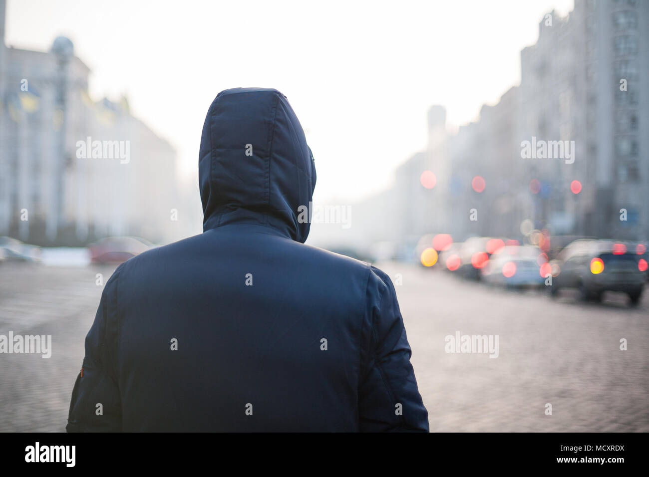 Lonely hipster man in hood walking on city street Stock Photo