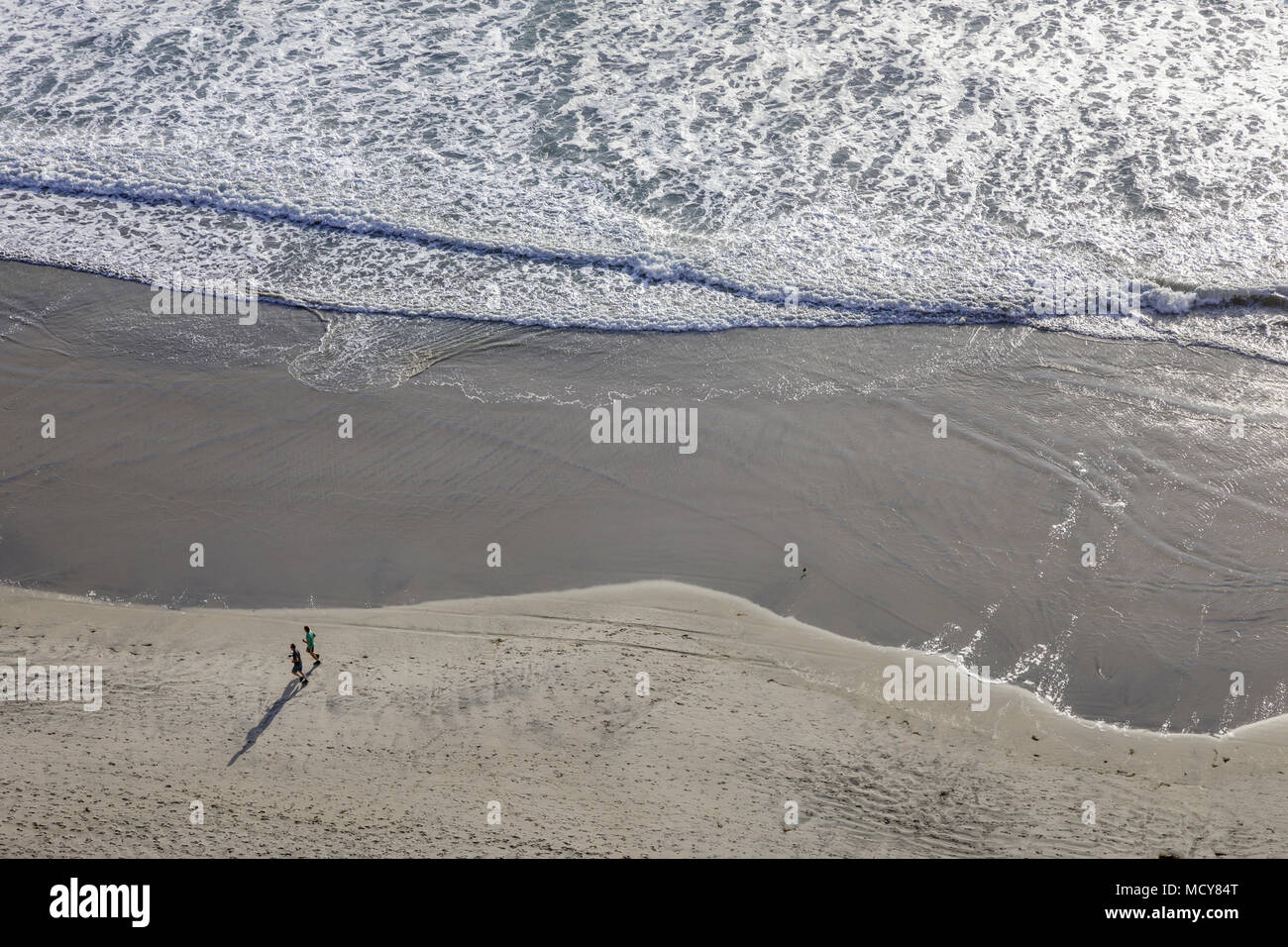 A high overhead view of a person walking along the beach with waves rolling in. Stock Photo