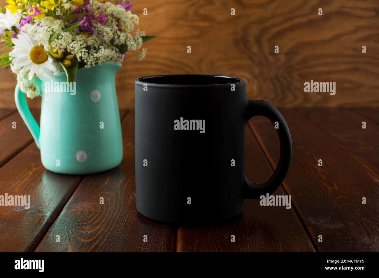 Black coffee mug rustic mockup with purple, yellow and white wildflowers in the mint green polka dot pitcher vase. Empty mug mock up for brand promoti Stock Photo