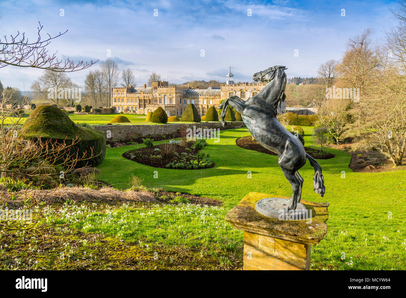 Winter sunshine lights up the facade of Forde Abbey with a rearing bronze horse statue and snowdrops in front, Dorset, England, UK Stock Photo