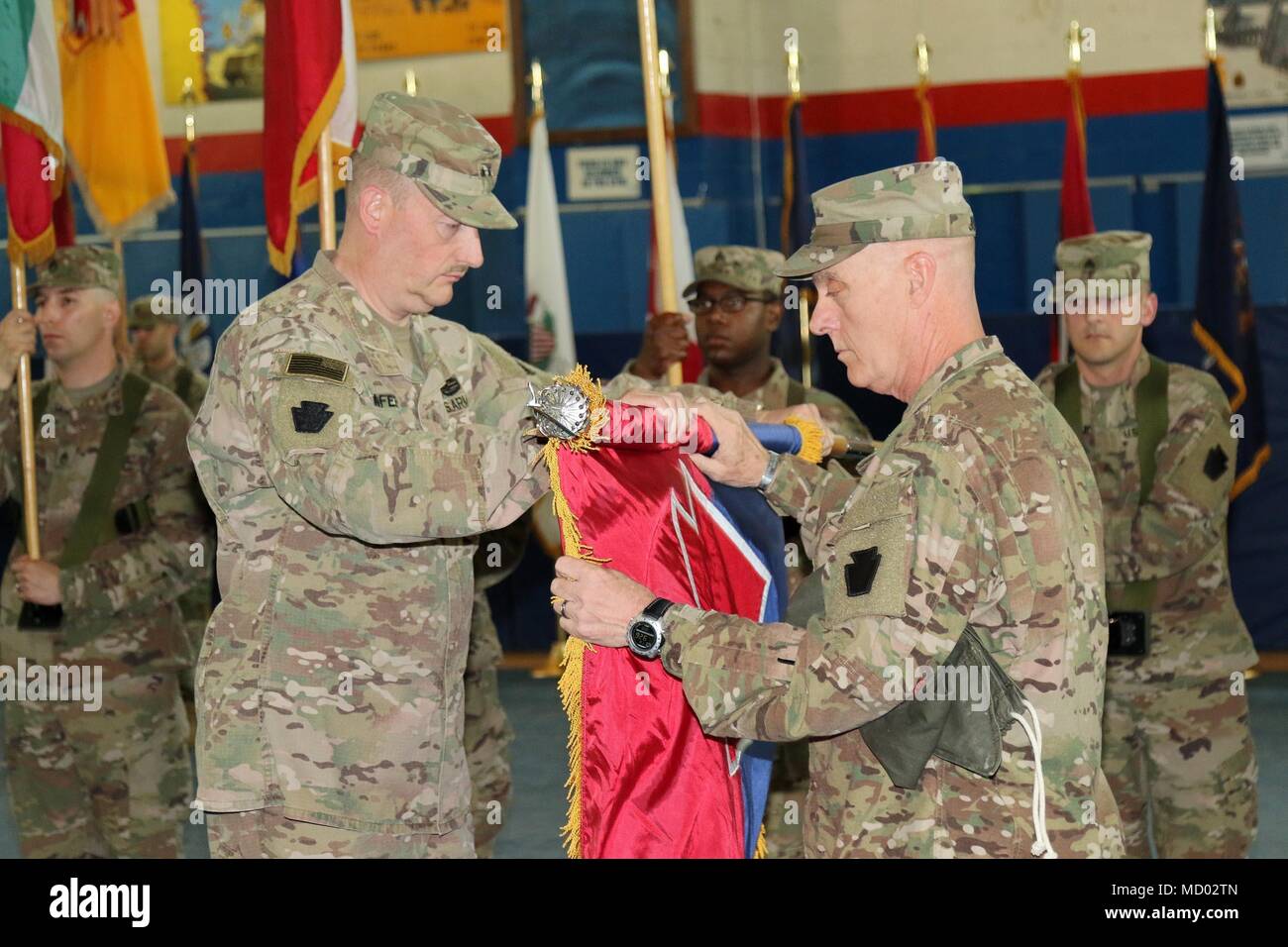CAMP ARIFJAN, Kuwait – Maj. Gen. Andrew Schafer (left), 28th Infantry Division commanding general, and Command Sgt. Maj. John Jones unfurl the division colors during a transfer of authority ceremony March 8, 2018. The Pennsylvania Army National Guard unit’s headquarters and headquarters battalion assumed responsibility from its counterpart, the 35th Infantry Division which is comprised of soldiers from the Missouri and Kansas National Guard. The 28th’s HHBN will serve as a division headquarters for roughly 10,000 soldiers conducting theater security operations in the Middle East. (U.S. Army ph Stock Photo