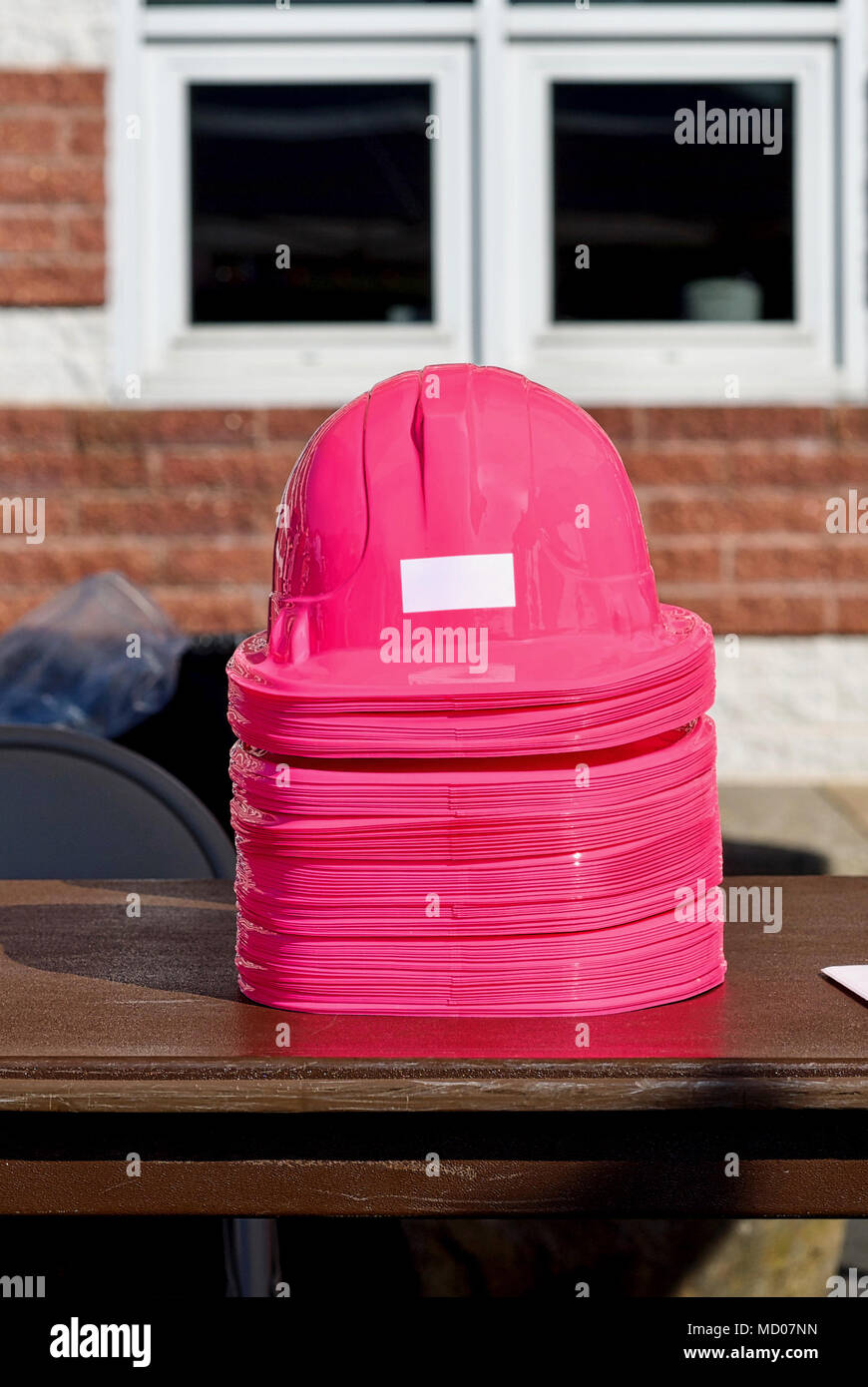 A stacked pile of pink plastic hardhats on a table. Stock Photo
