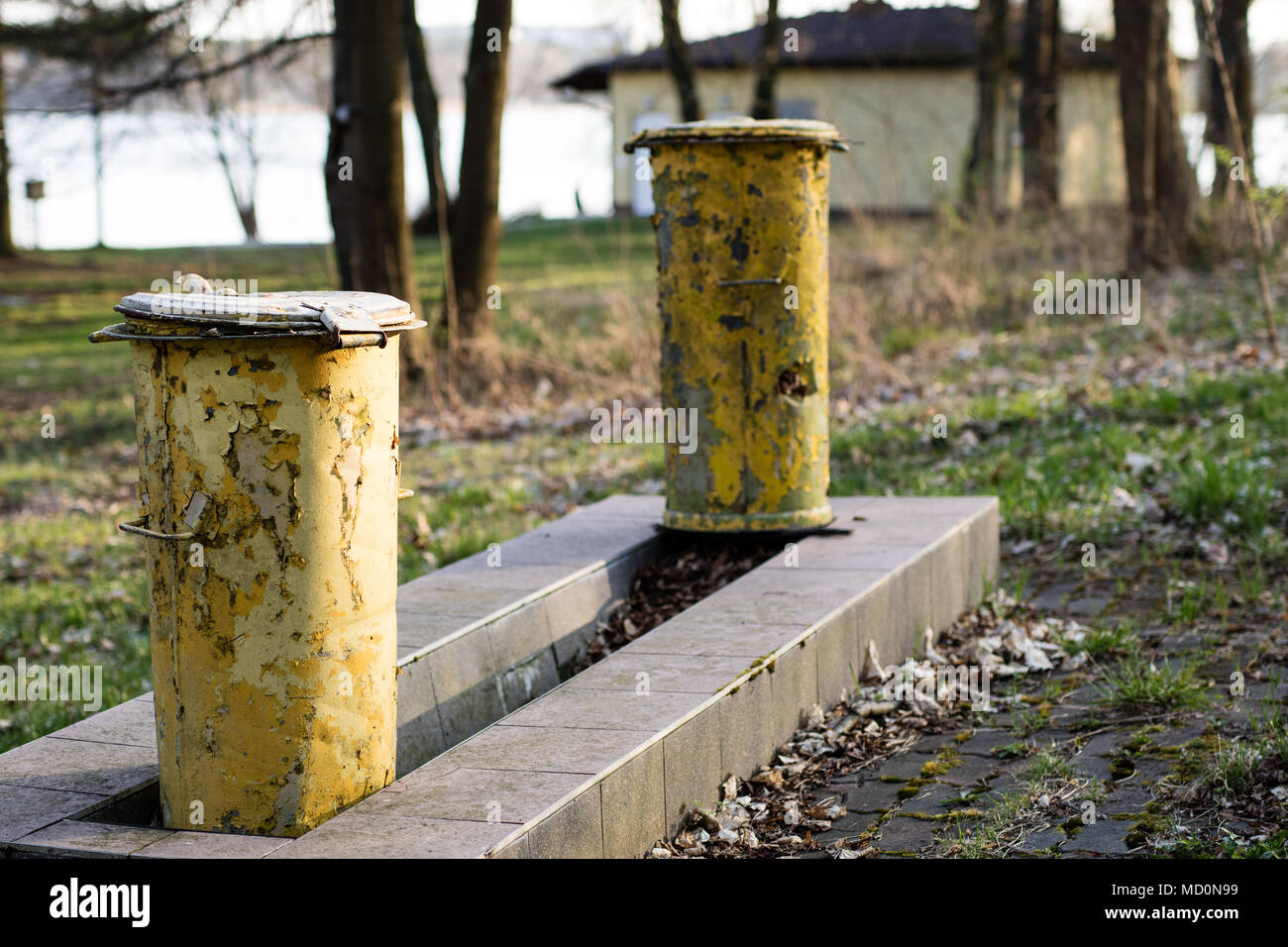 An old garbage bin. Waste trash cans set in a park between trees on a concrete foundation