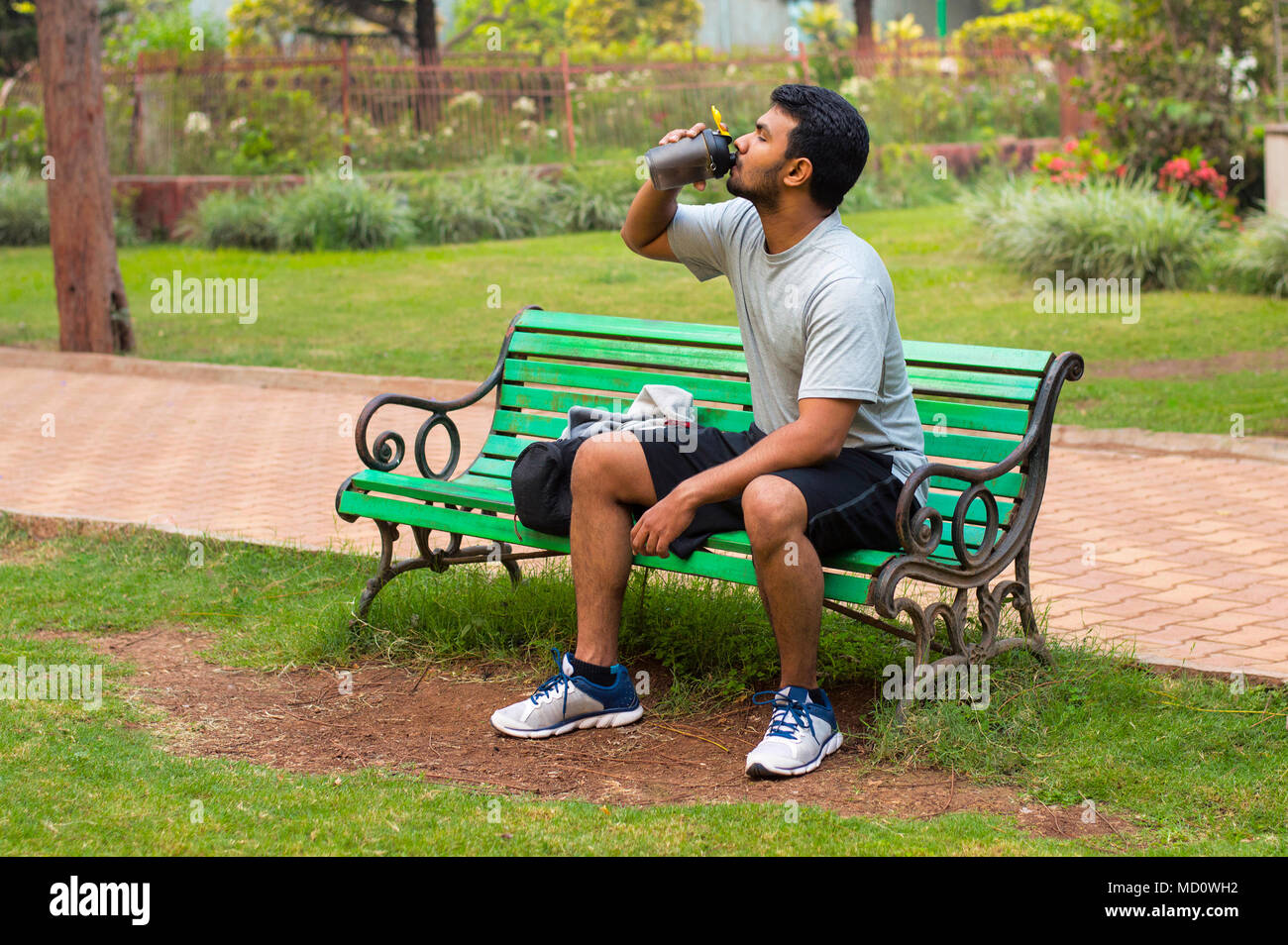 Young athlete drinking water while resting in park bench Stock Photo