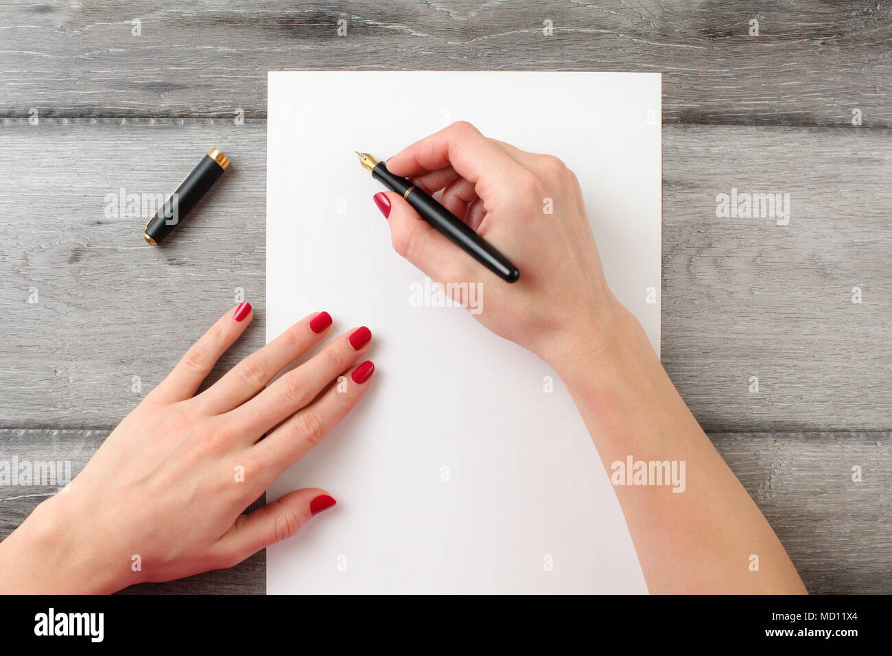 View from above to woman's hands with red nails, holding black fountain ink pen with gold nib, ready to write something on empty piece of paper laying Stock Photo