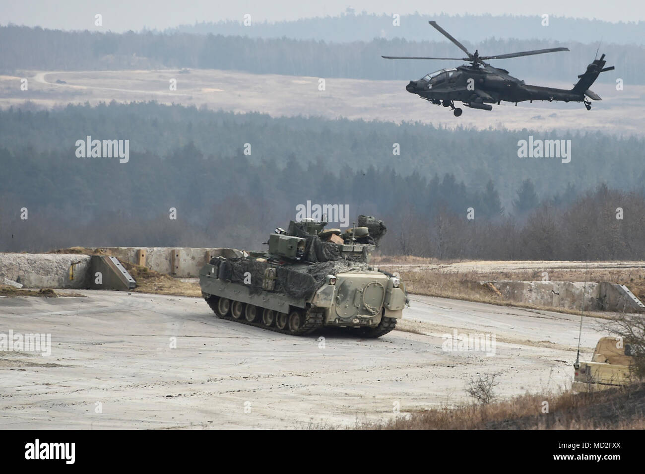 An AH-64D Apache Longbow helicopter with Task Force Viper 1st Battalion, 3rd Aviation Regiment, 12th Combat Aviation Brigade provides air support for a Bradley Fighting Vehicle with 5th Squadron, 4th Cavalry Regiment, 2nd Armored Brigade Combat Team, 1st Infantry Division during a combined arms live fire exercise at the 7th Army Training Command’s Grafenwoehr Training Area, Germany, March 26, 2018. Stock Photo