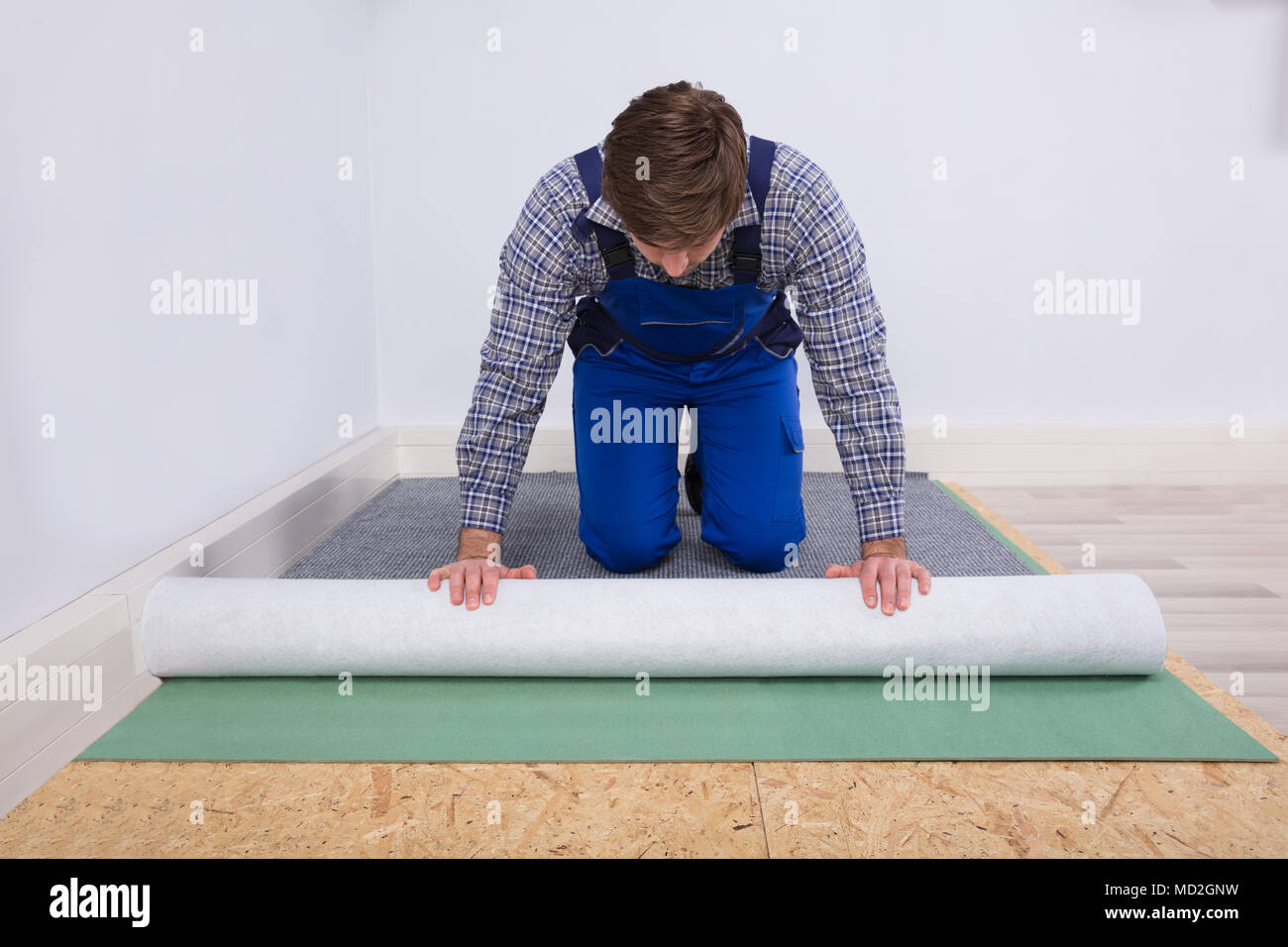 Side View Of A Young Male Worker In Overalls Installing Carpet Stock Photo