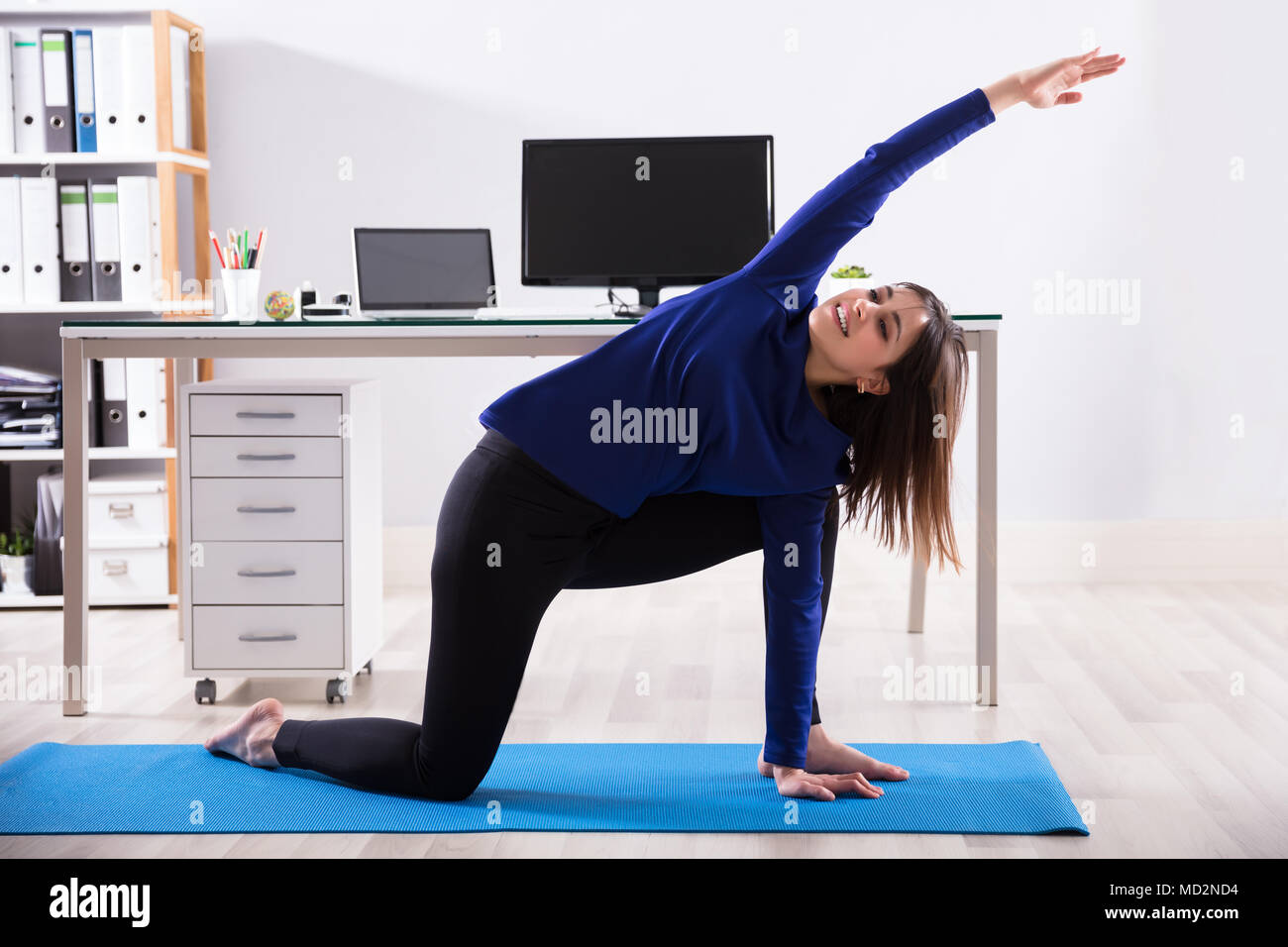 Side View Of A Young Businesswoman Doing Workout On Exercise Mat In Office Stock Photo
