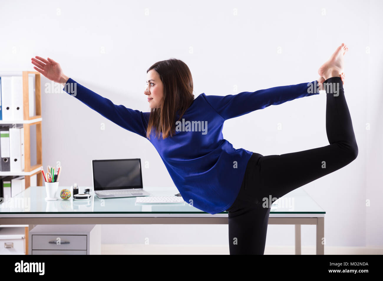 Young Businesswoman Looking At Invoice On Computer Doing Yoga Stock Photo