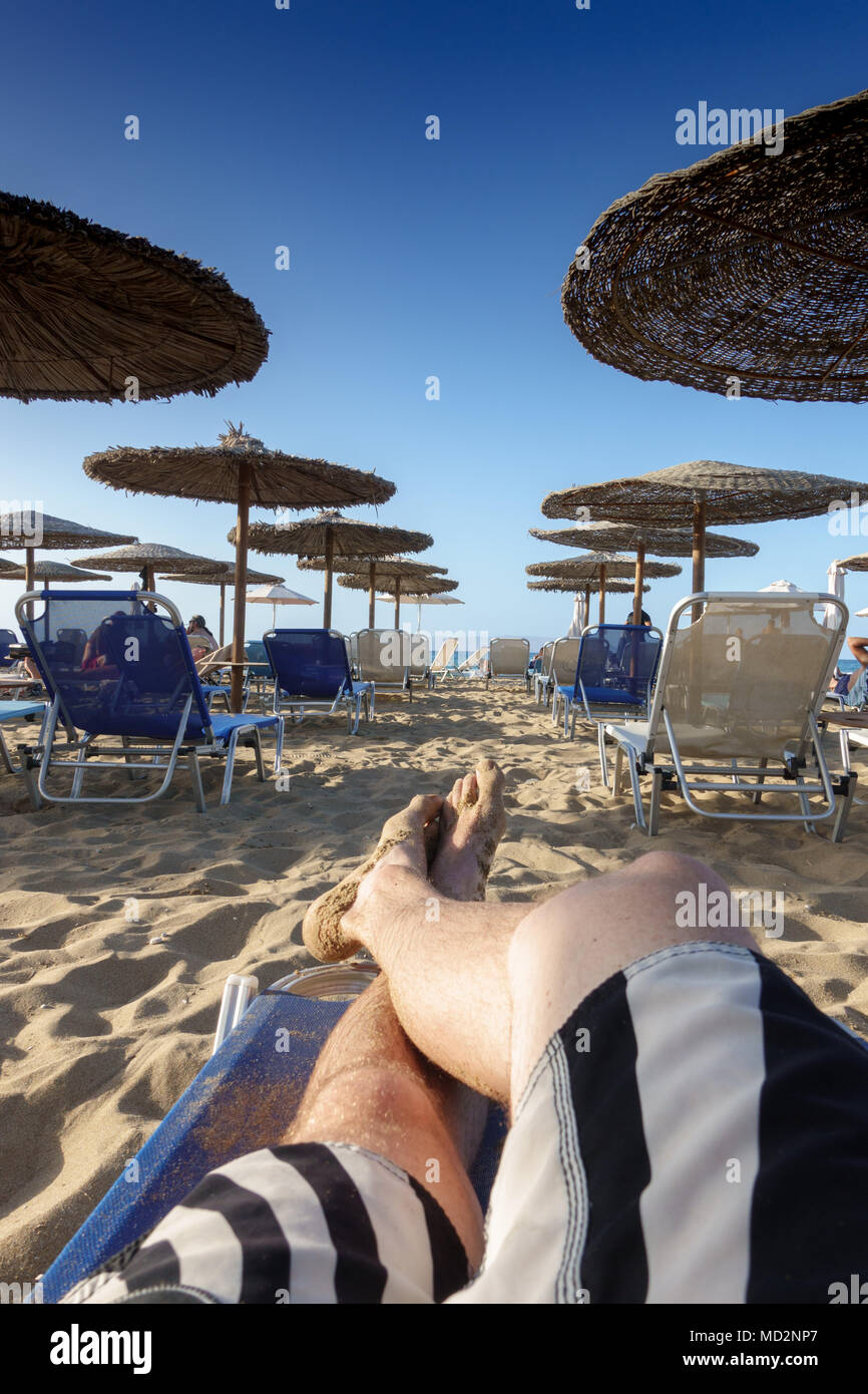 Low section of barefoot man relaxing on sandy beach lounge chair Stock Photo